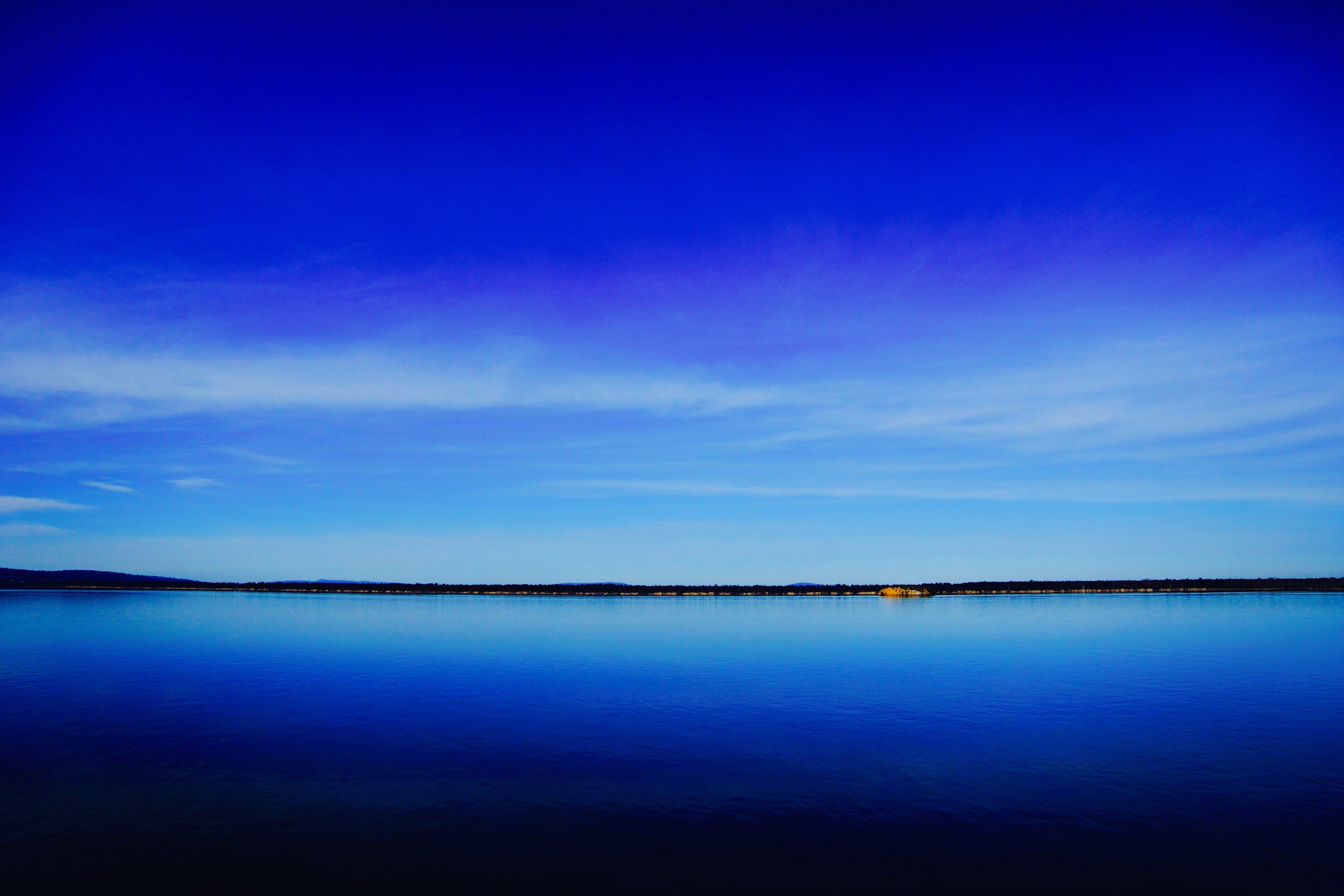 3840x2560 Wallpaper / a deep blue lake and clear sky separated by a dark green shoreline on the horizon, blue lake under blue sky 4k wallpaper free download