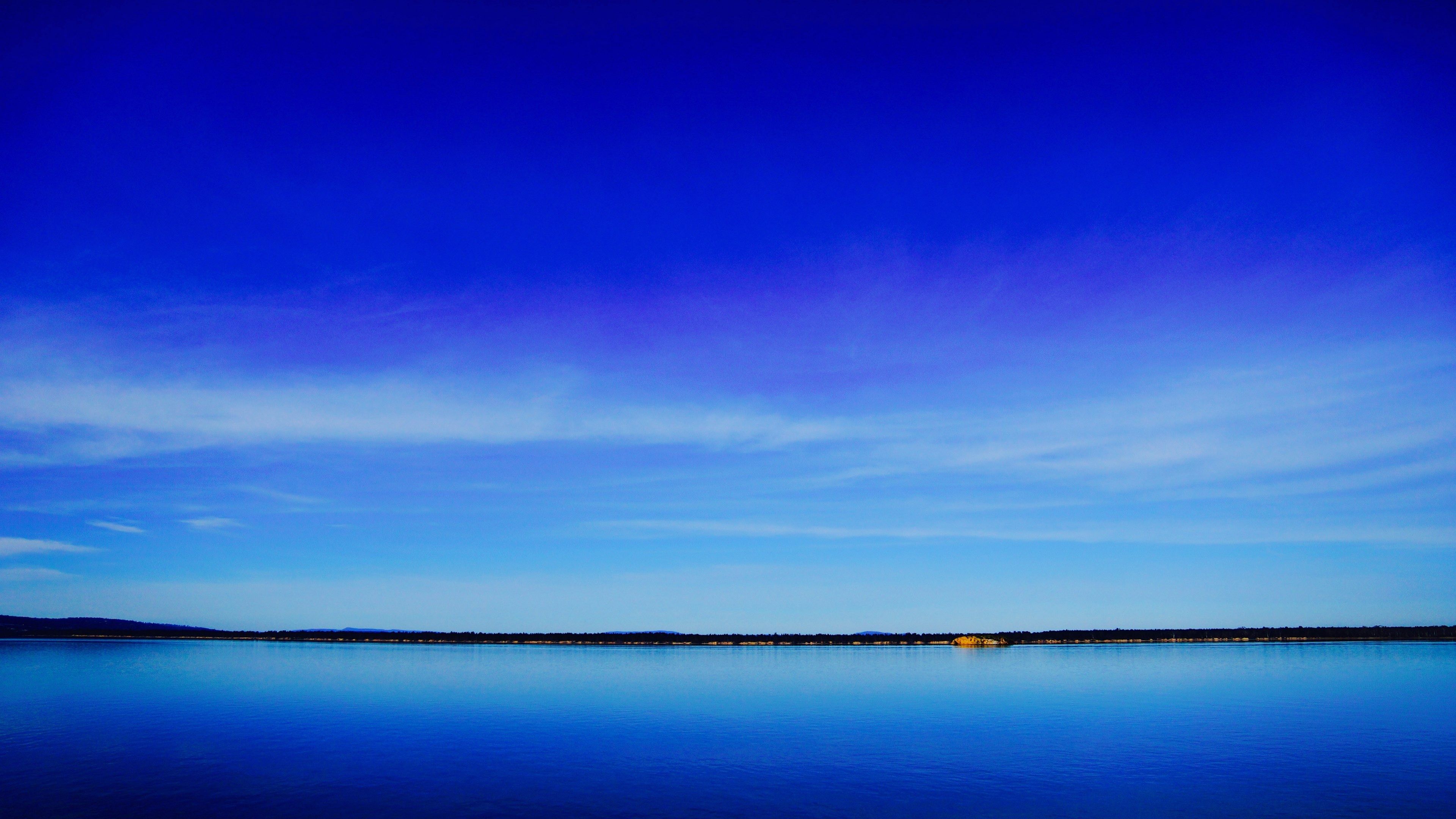 3840x2160 Wallpaper / a deep blue lake and clear sky separated by a dark green shoreline on the horizon, blue lake under blue sky 4k wallpaper free download