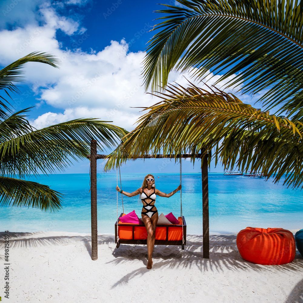 1000x1000 Beautiful tanned woman in elegant bikini on Maldives island. Young glamor girl is posing on swing in paradise. Perfect body bikini model on Maldives beach. Bikini fashion. Luxury travel
