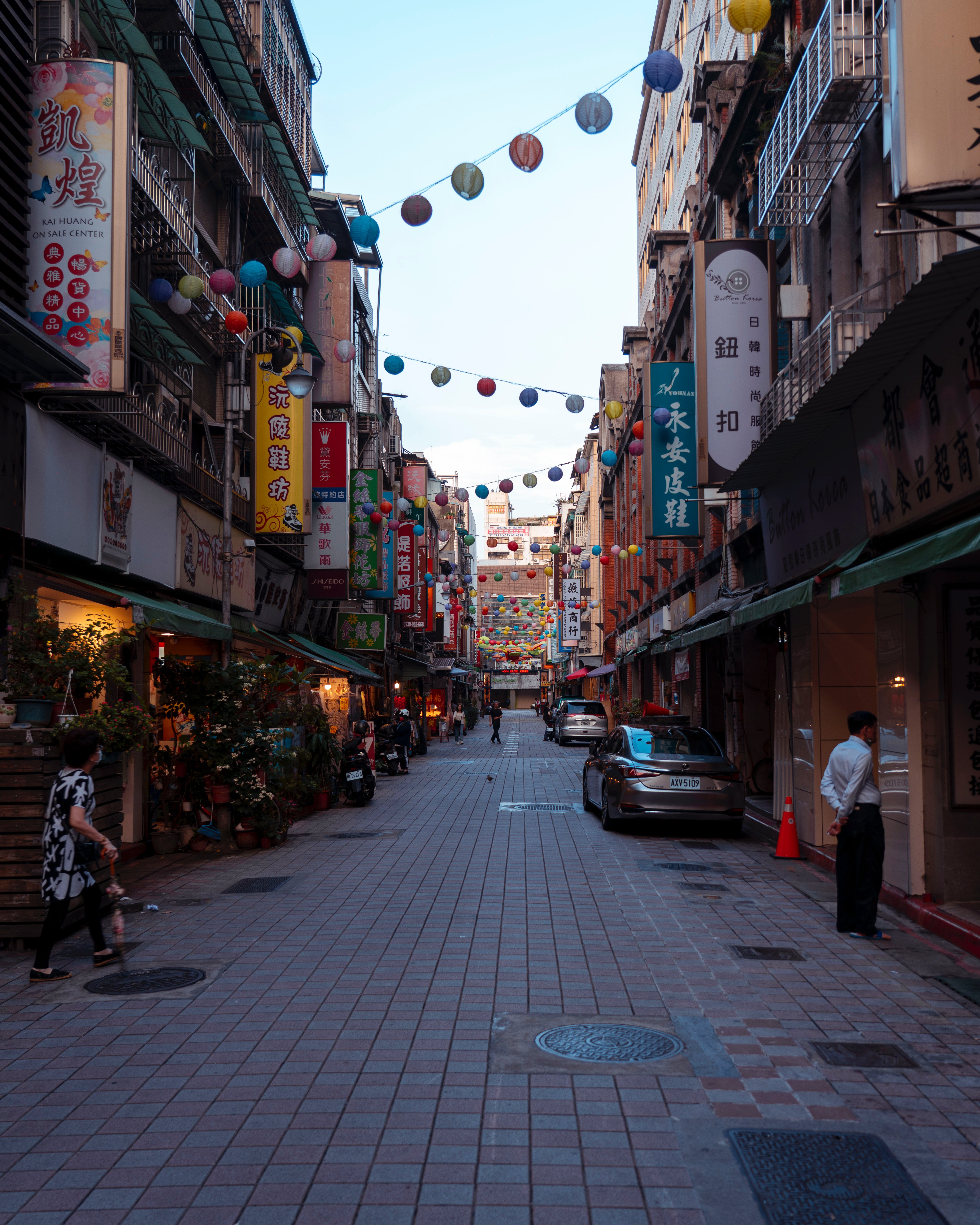 5125x6406 Couple Walking along Asian Narrow Street with Shops in Big City · Free