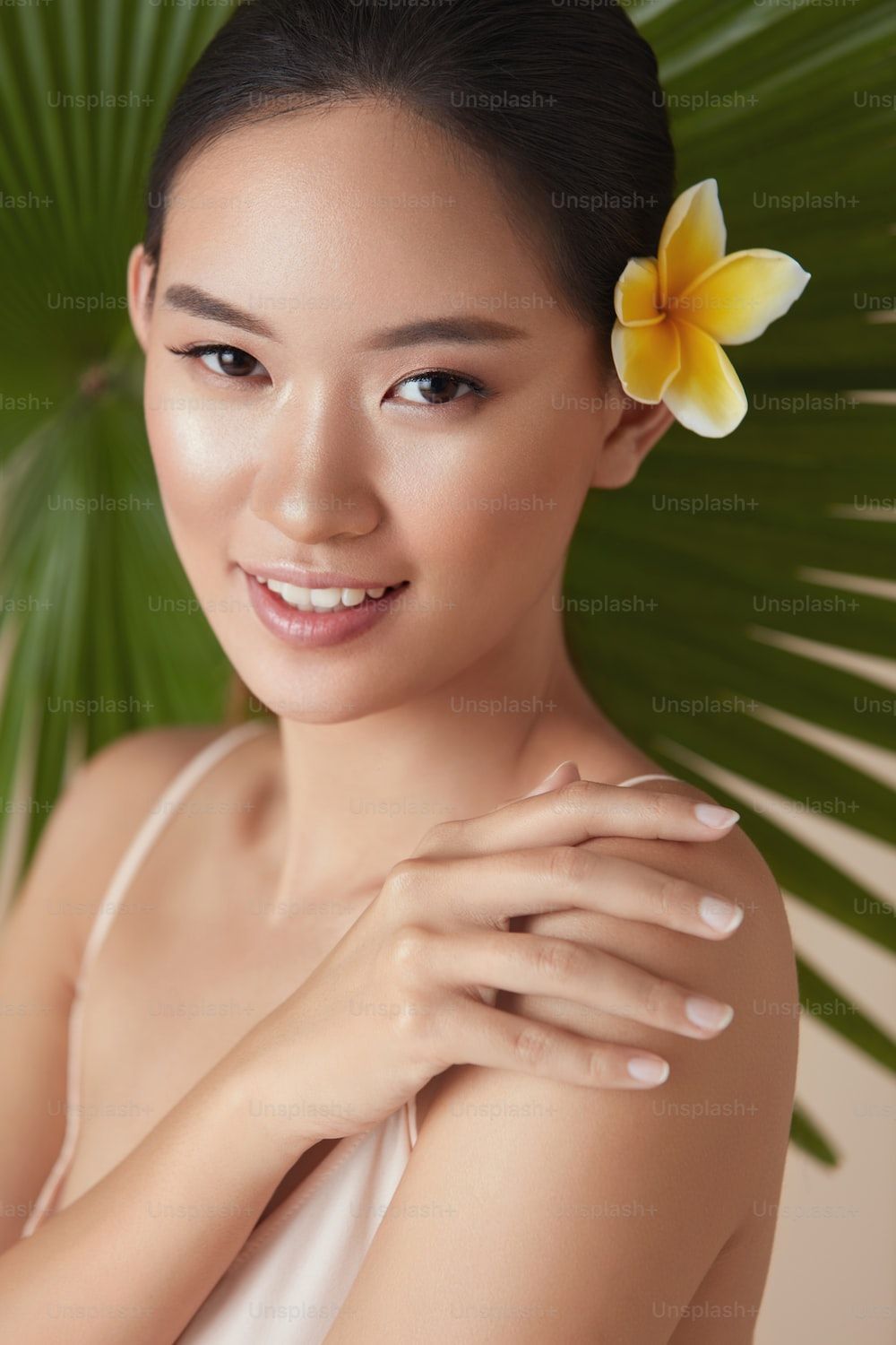 1000x1500 Beauty. Model Near Palm With Flower In Hair. Tender Asian Woman Touching Shoulder Portrait On Tropical Plant Background. Beautiful Girl Enjoying Hydrated Skin After Using Natural Organic Cosmetic. photo