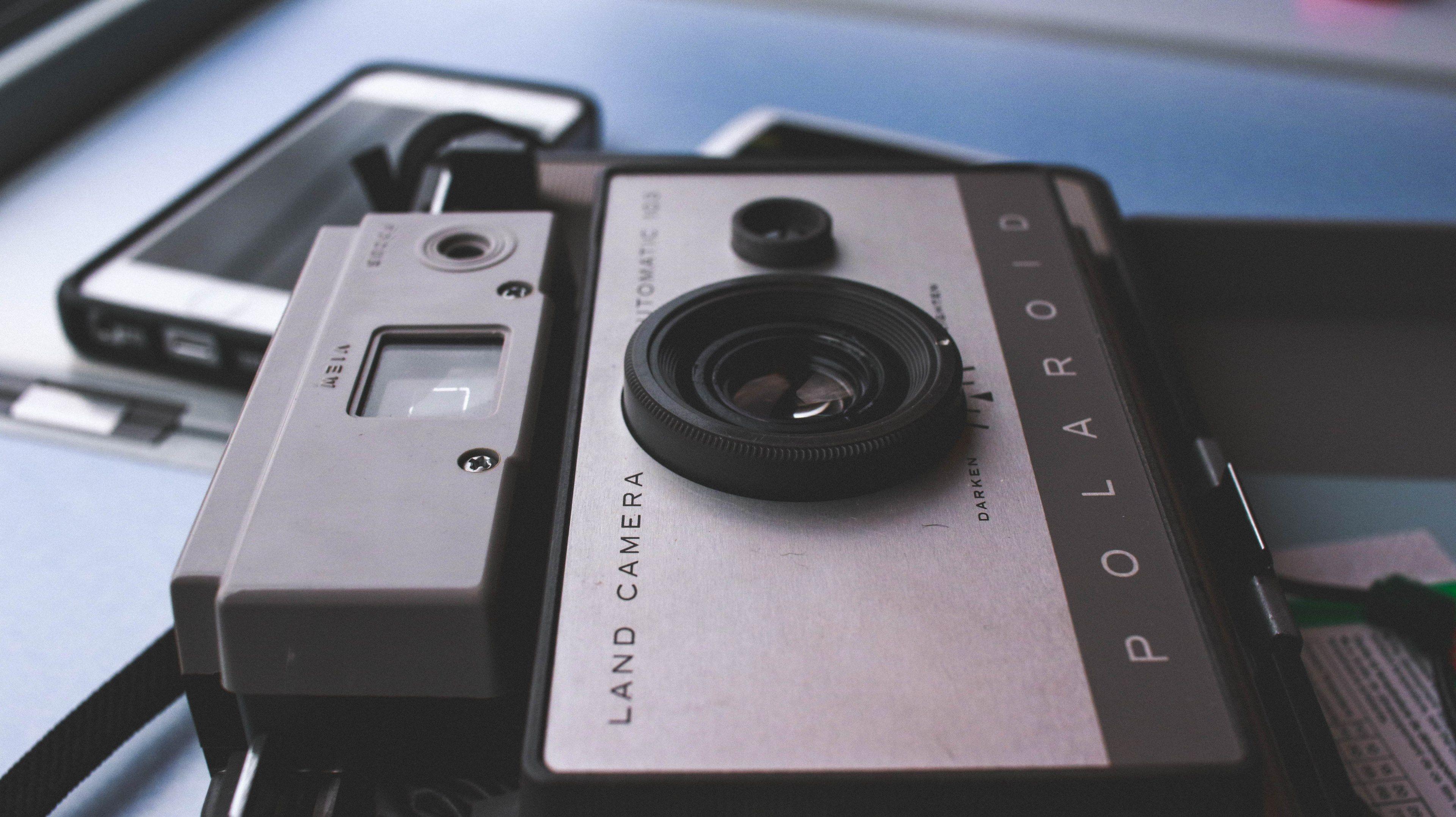 3840x2156 macro of vintage polaroid camera on surface near iphone