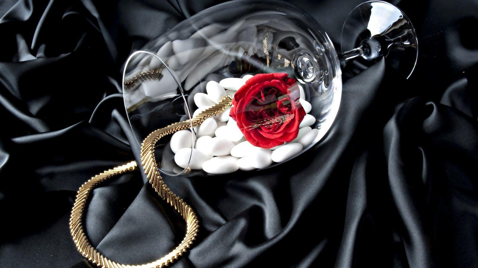 1600x900 A glass with a gold chain, a red rose and white stones on a