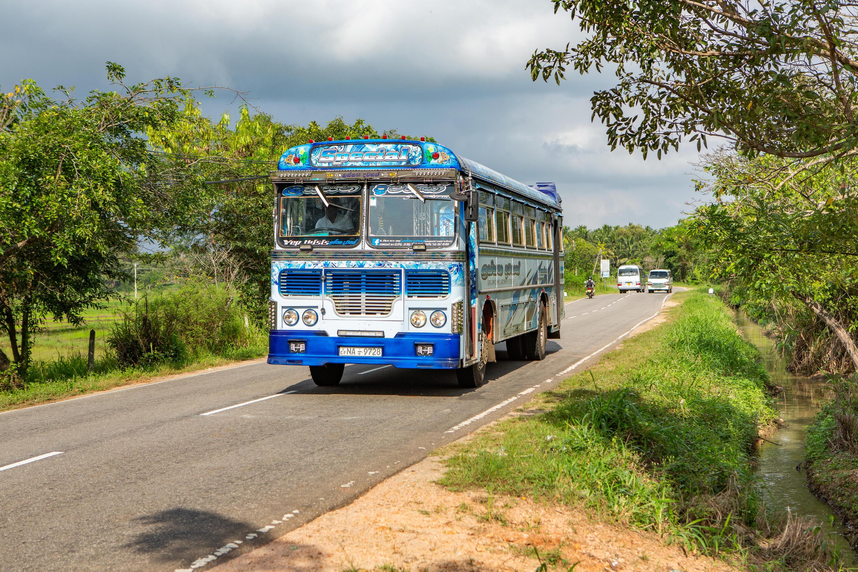 2940x1960 Dambulla, Sri Lanka, 08 january 2025 Traditional Sri Lankan bus driving on a winding coastal road with the Indian Ocean in the background