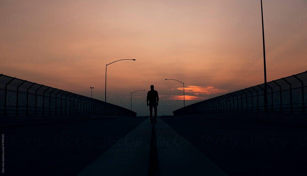 1200x689 Silhouetted man walking alone across a bridge