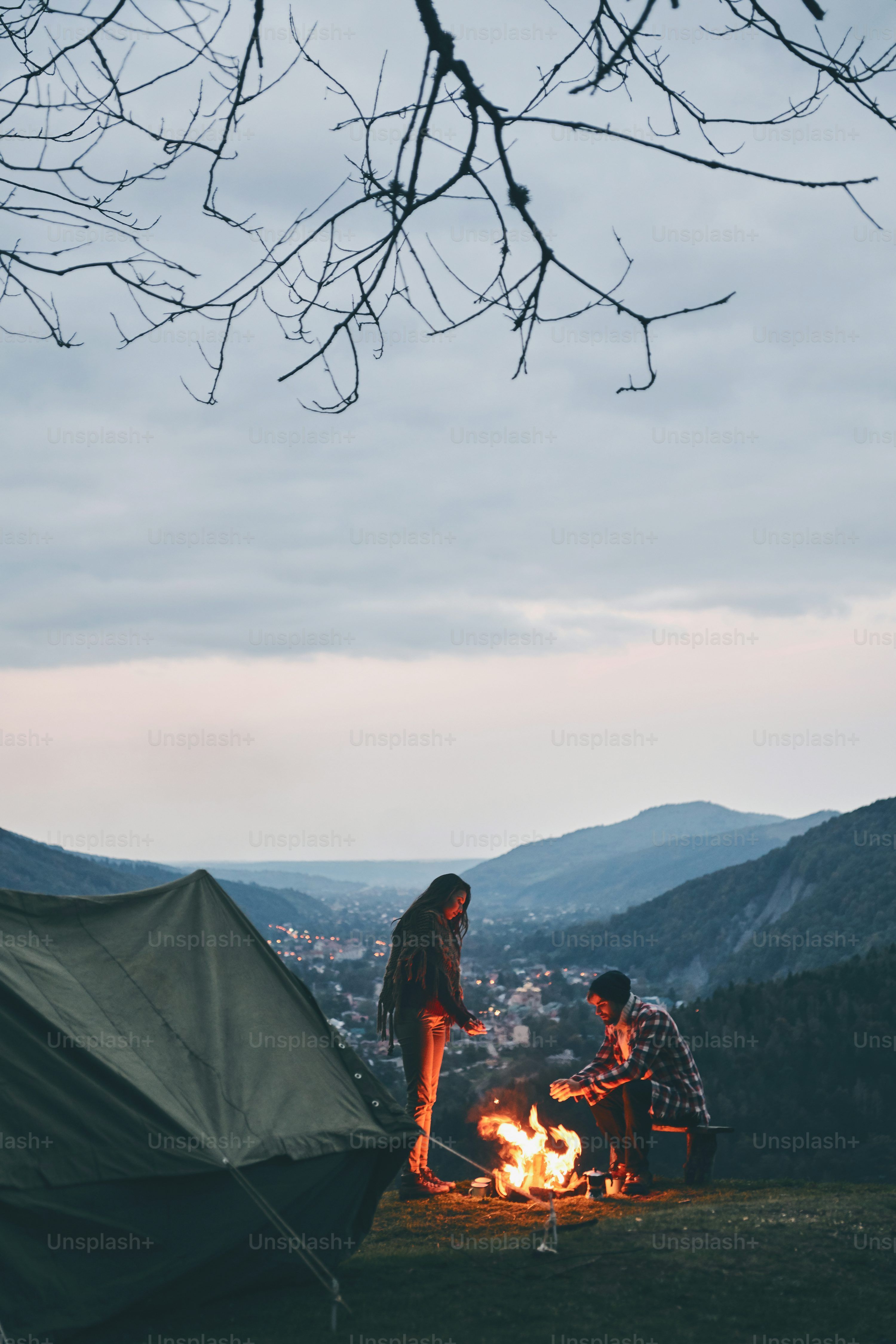 3000x4498 Beautiful young couple warming up by the campfire while camping in the mountains photo
