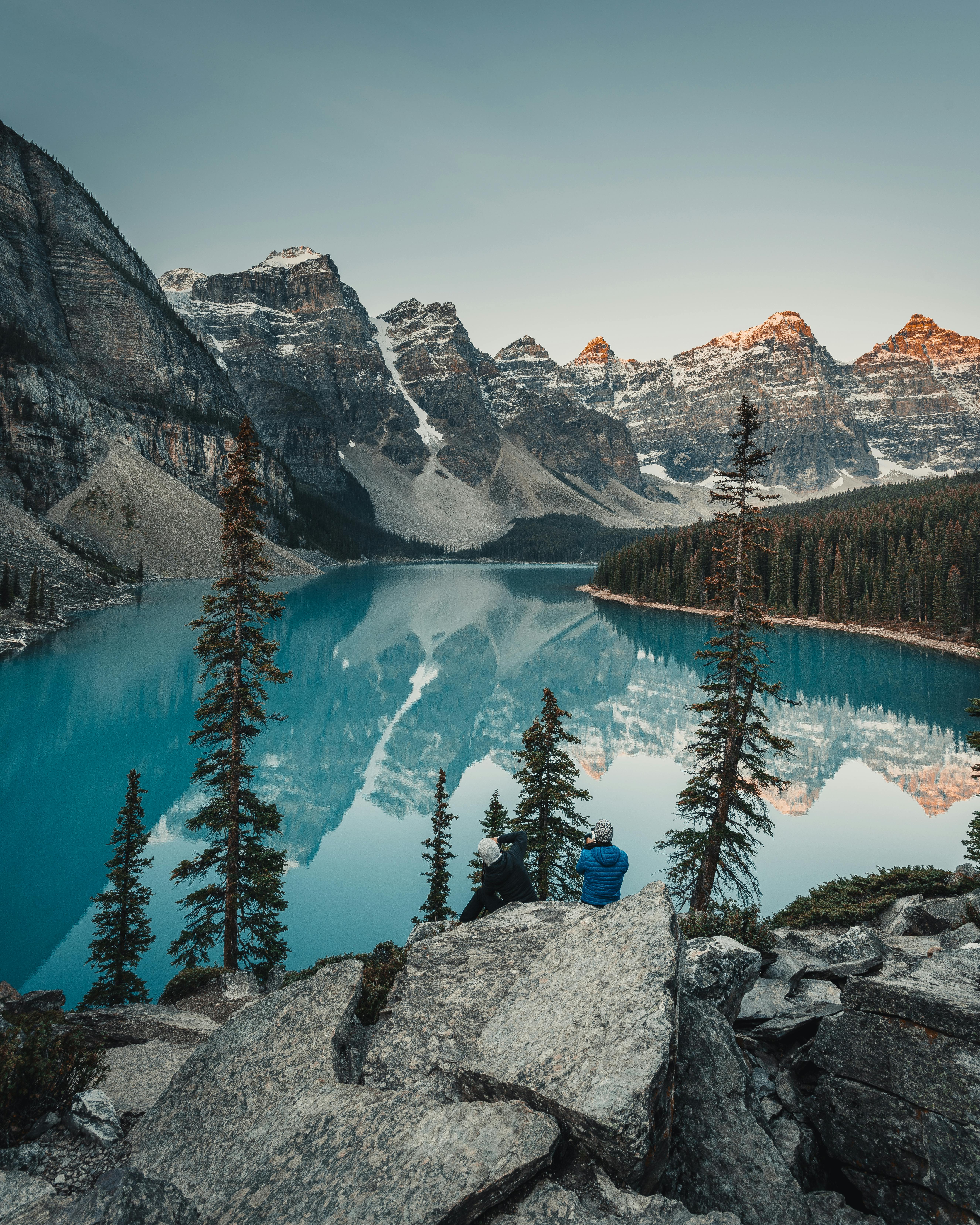 5304x6630 Two People Sitting on a Cliff Overlooking the Scenic View of a Placid Lake Across the Mountains · Free