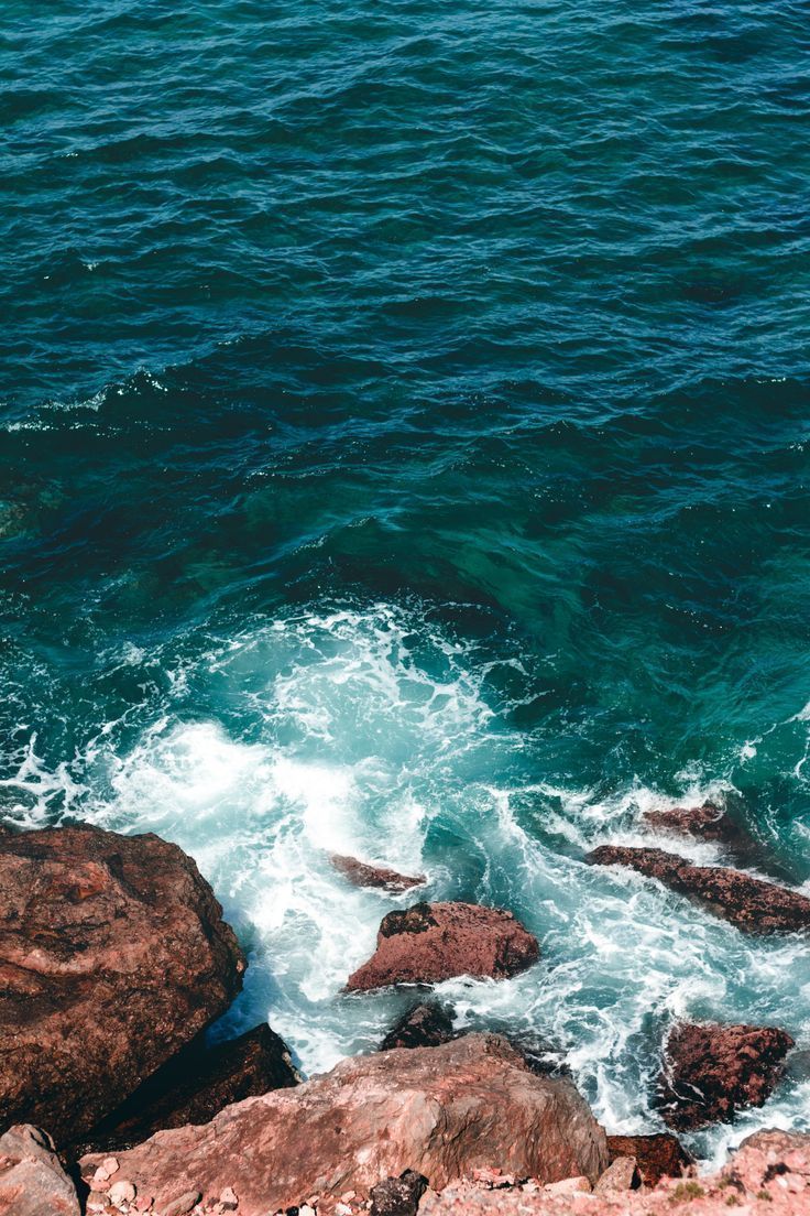 736x1104 Beautiful dark turquoise sea water splashing on brown sea rock