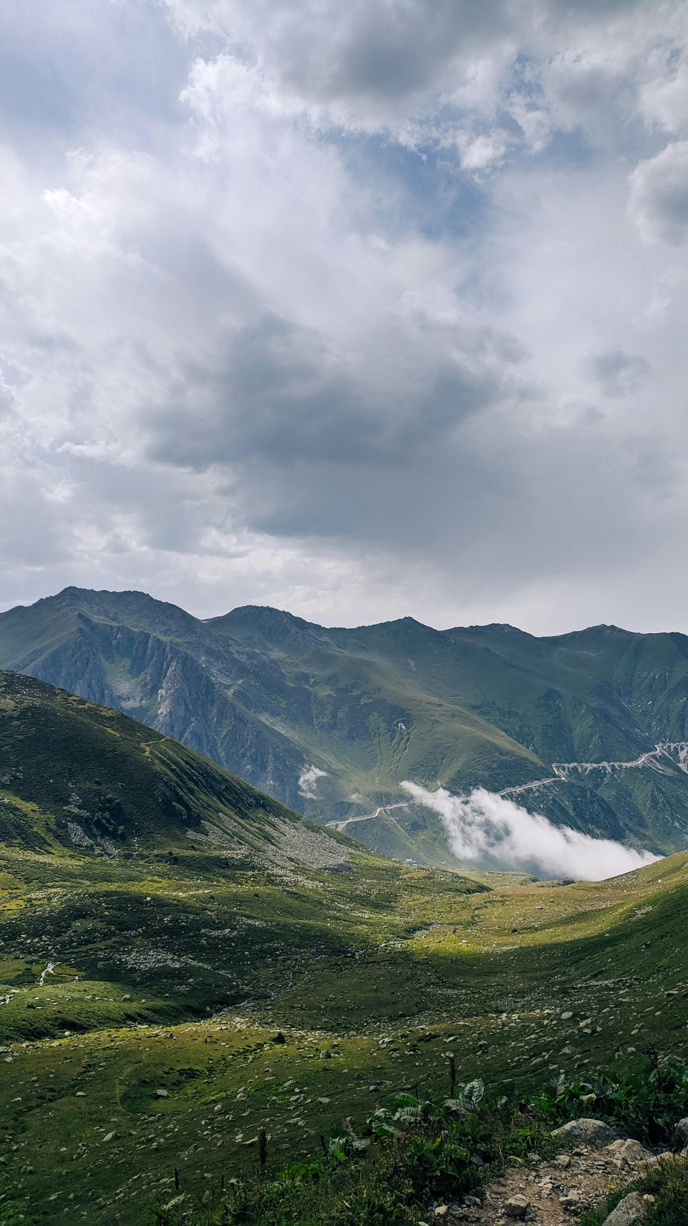 2246x3998 Landscape of Grass Field in Mountains and Mountain Range under a Cloudy Sky · Free