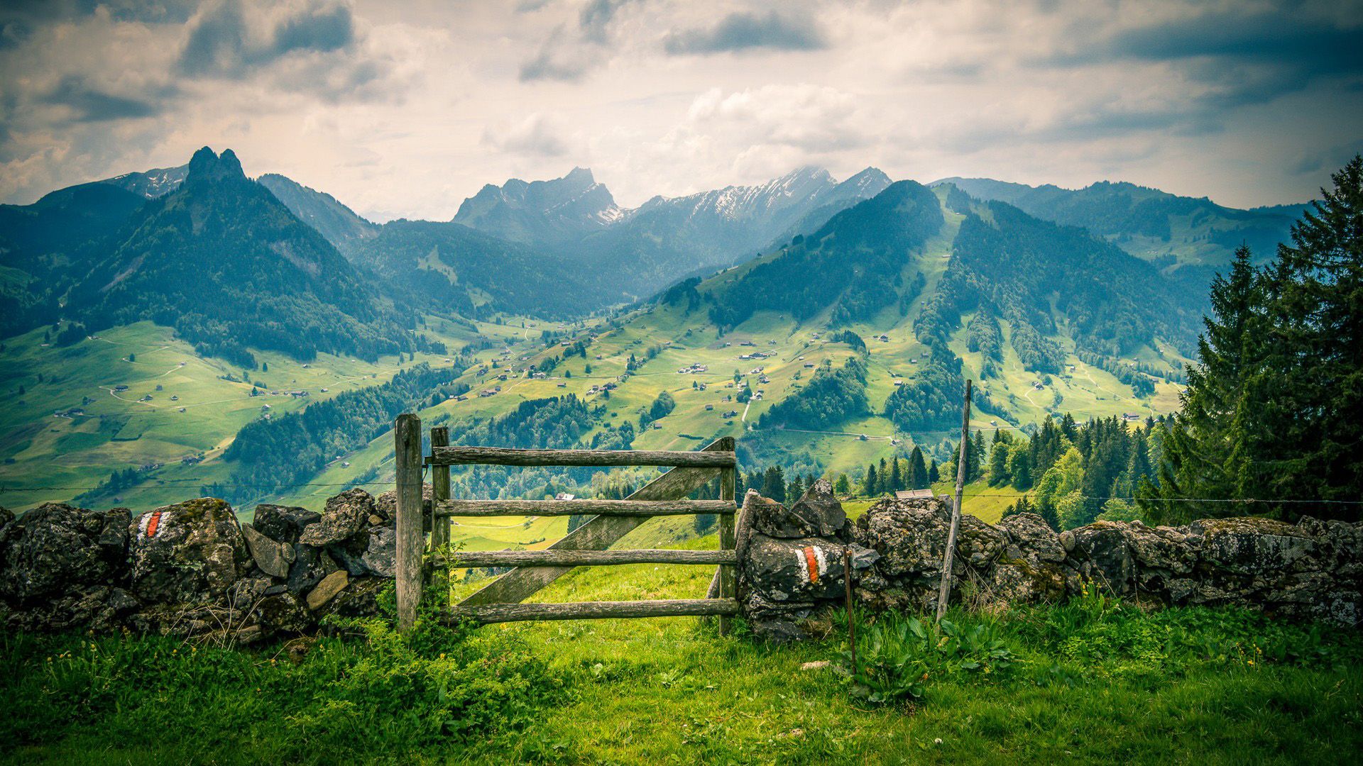 1920x1080 Landscape Spring Mountains Villages Green Grass Field Fence Cloudy Sky Background HD Nature Wallpaper
