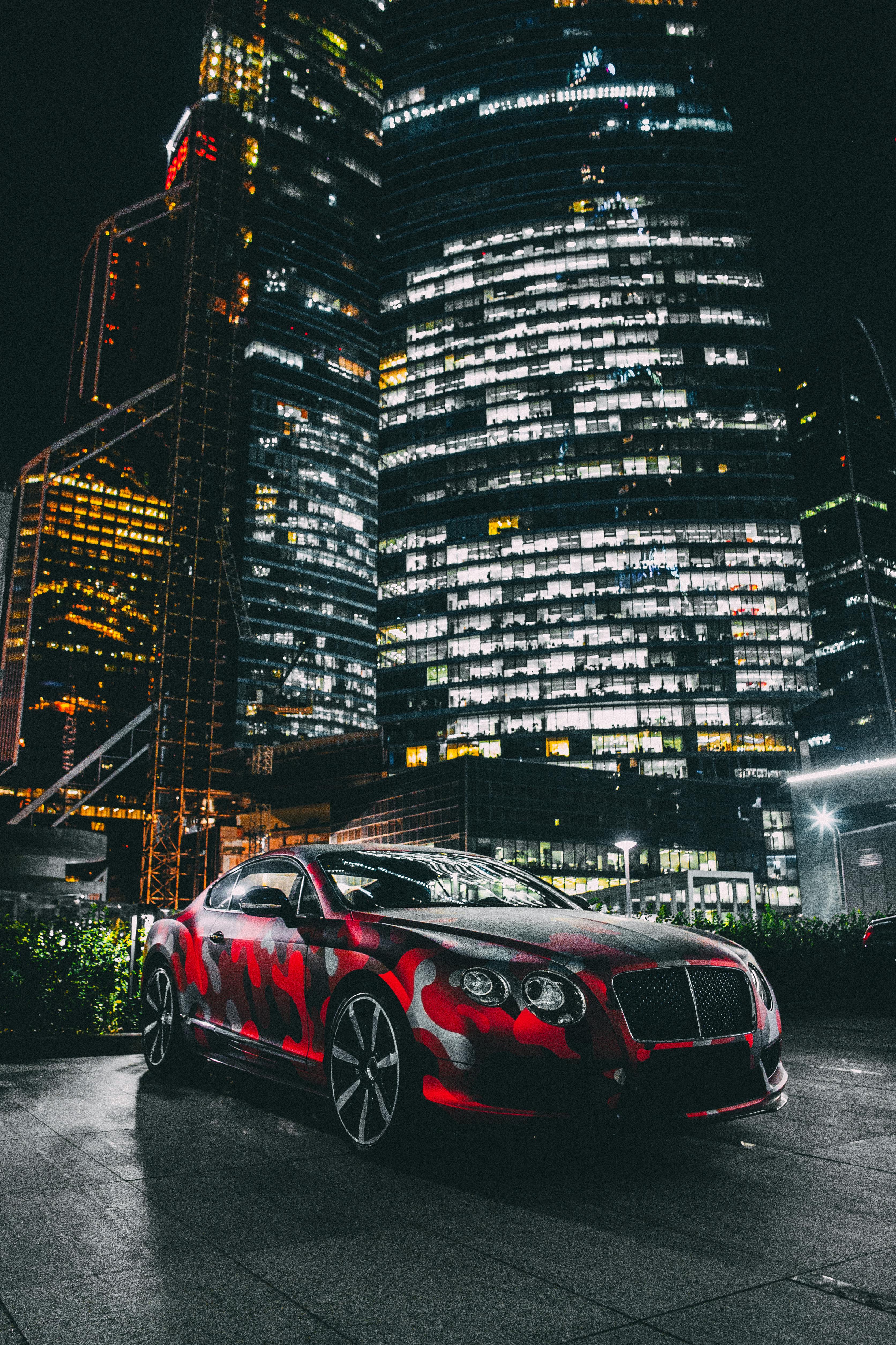 3344x5016 Bentley Continental GT Parked in front of Illuminated Skyscrapers in Modern Downtown · Free