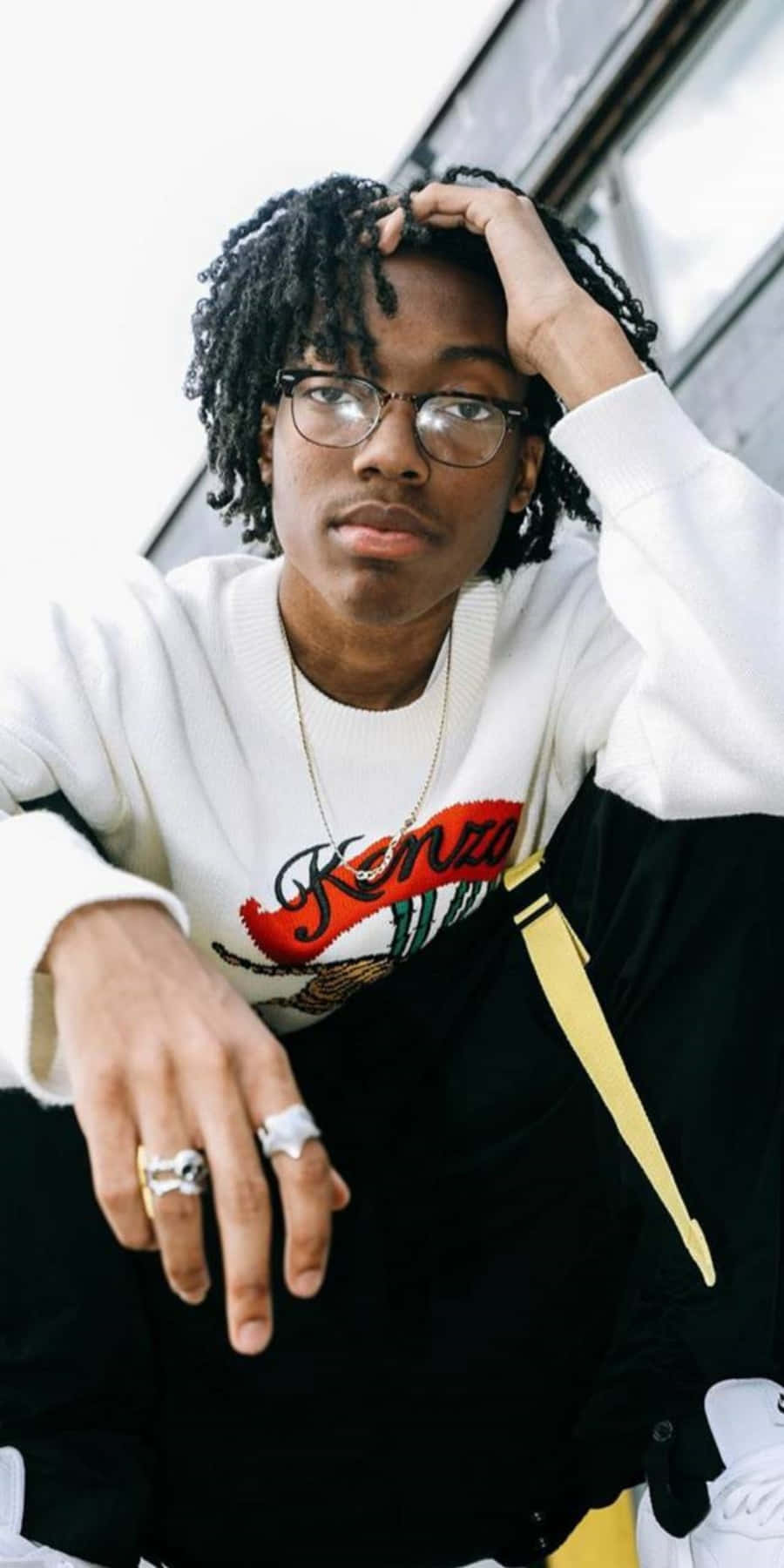 900x1800 Download A Young Man With Dreadlocks And Glasses Sitting On A Ledge Wallpaper