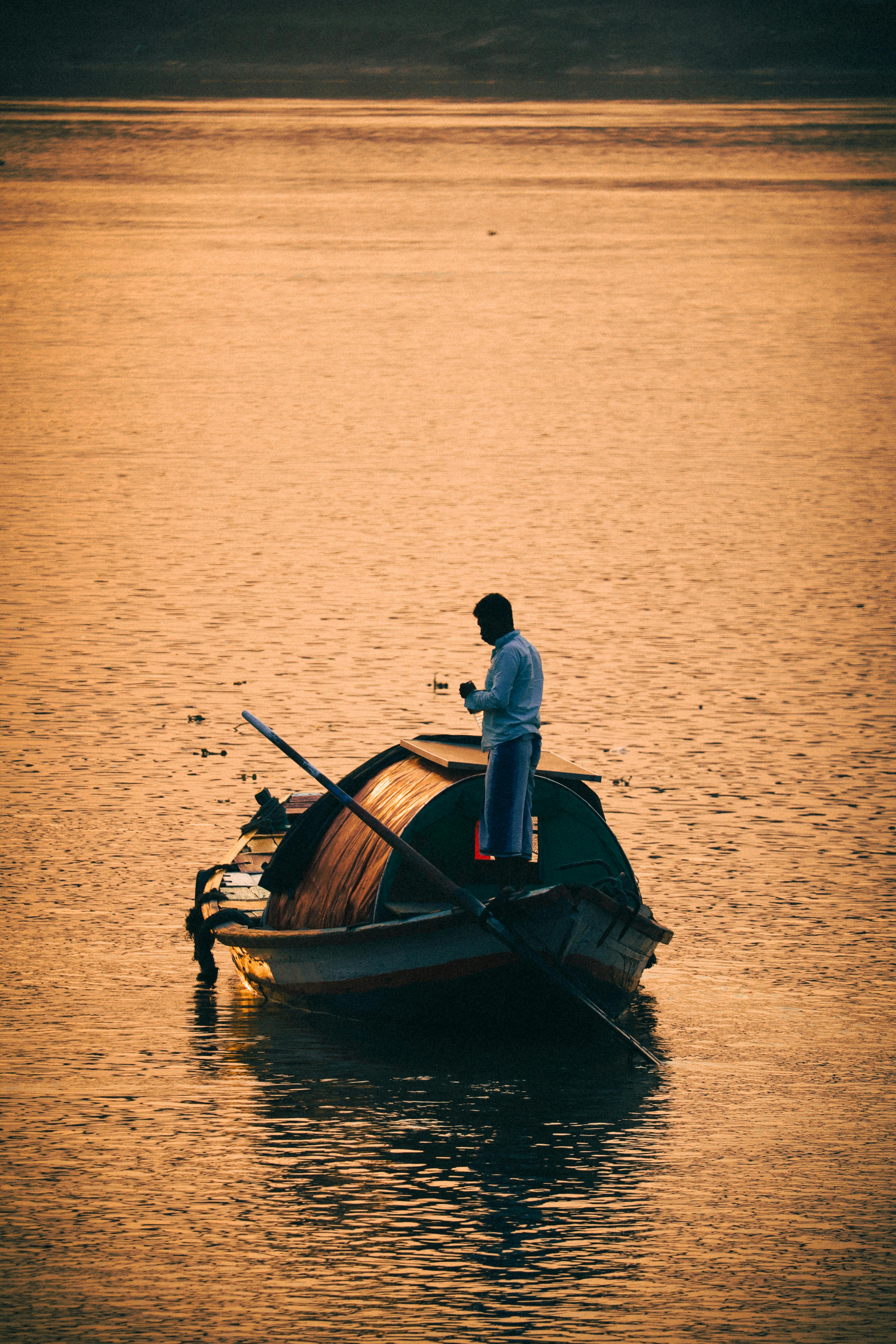 3967x5950 Man Standing on a Small Wooden Boat at Sunrise · Free