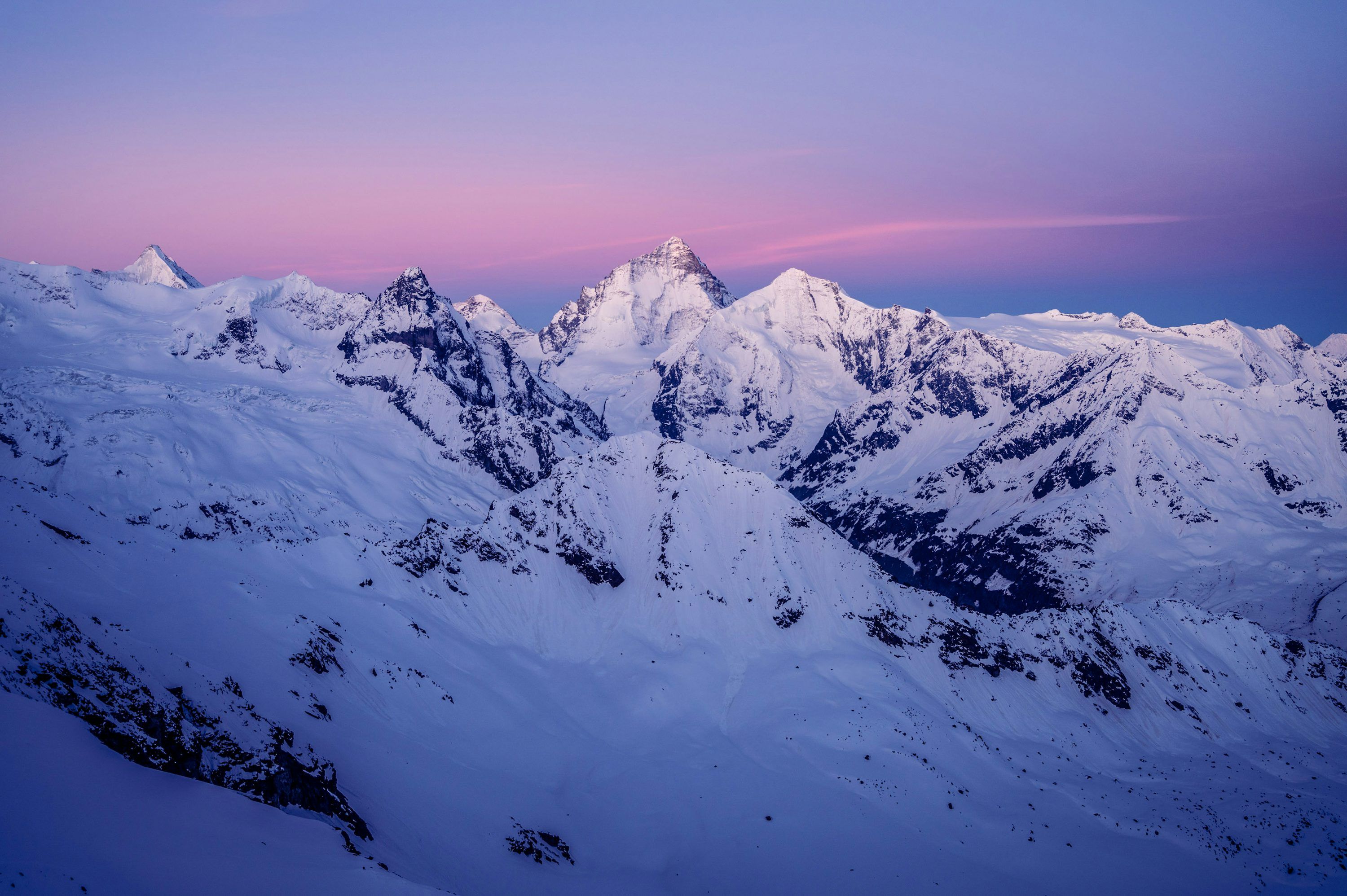 3000x1996 A snowy mountain range with a pink sky in the background photo