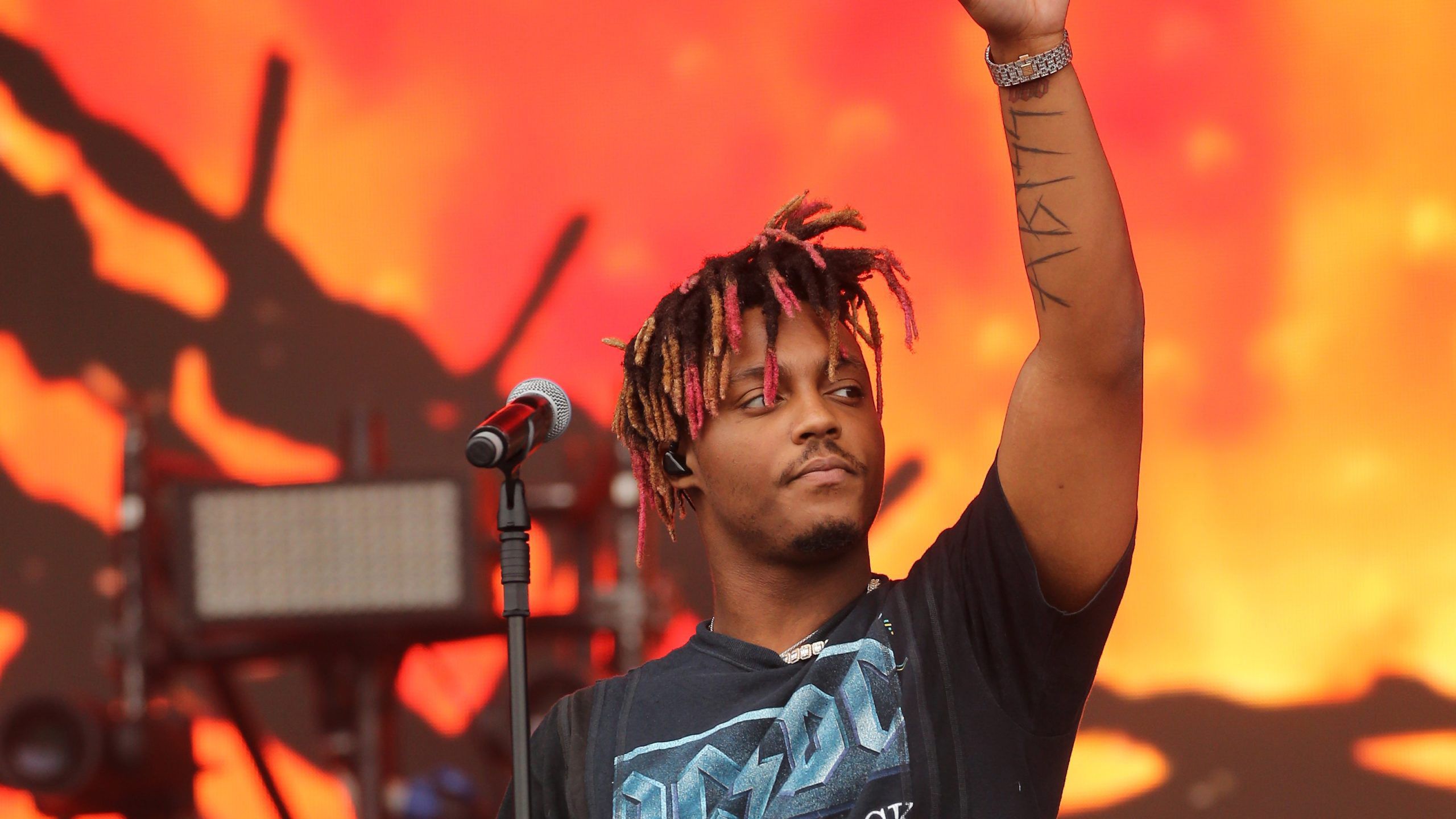 2560x1440 Juice Wrld Is Standing In Front Of Mike Wearing Black T Shirt Standing In Orange Yellow Background HD Juice Wrld Wallpaper