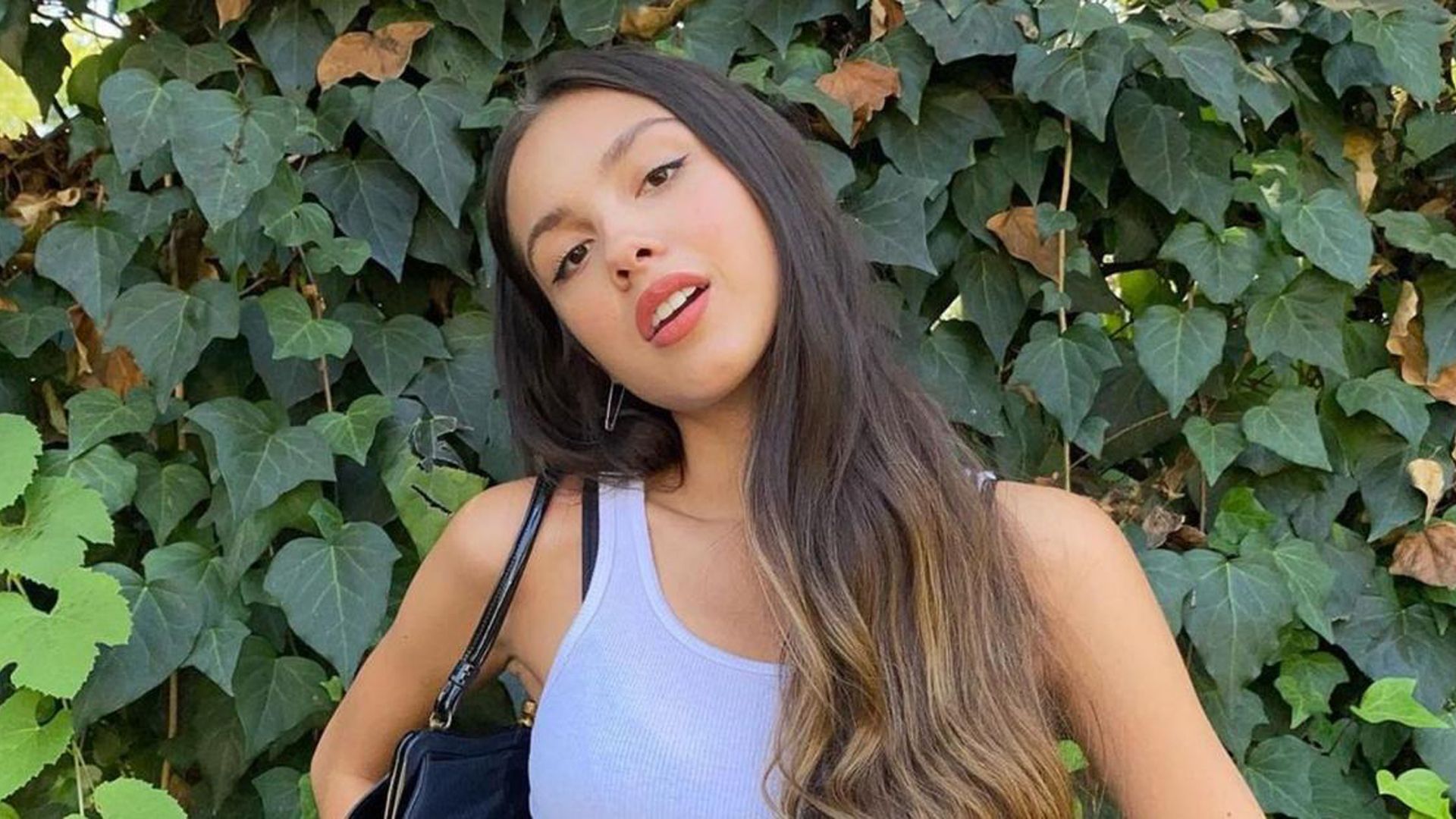 1920x1080 Olivia Rodrigo Is Standing In Green Leaves Background Wearing White Dress HD Girls Wallpaper