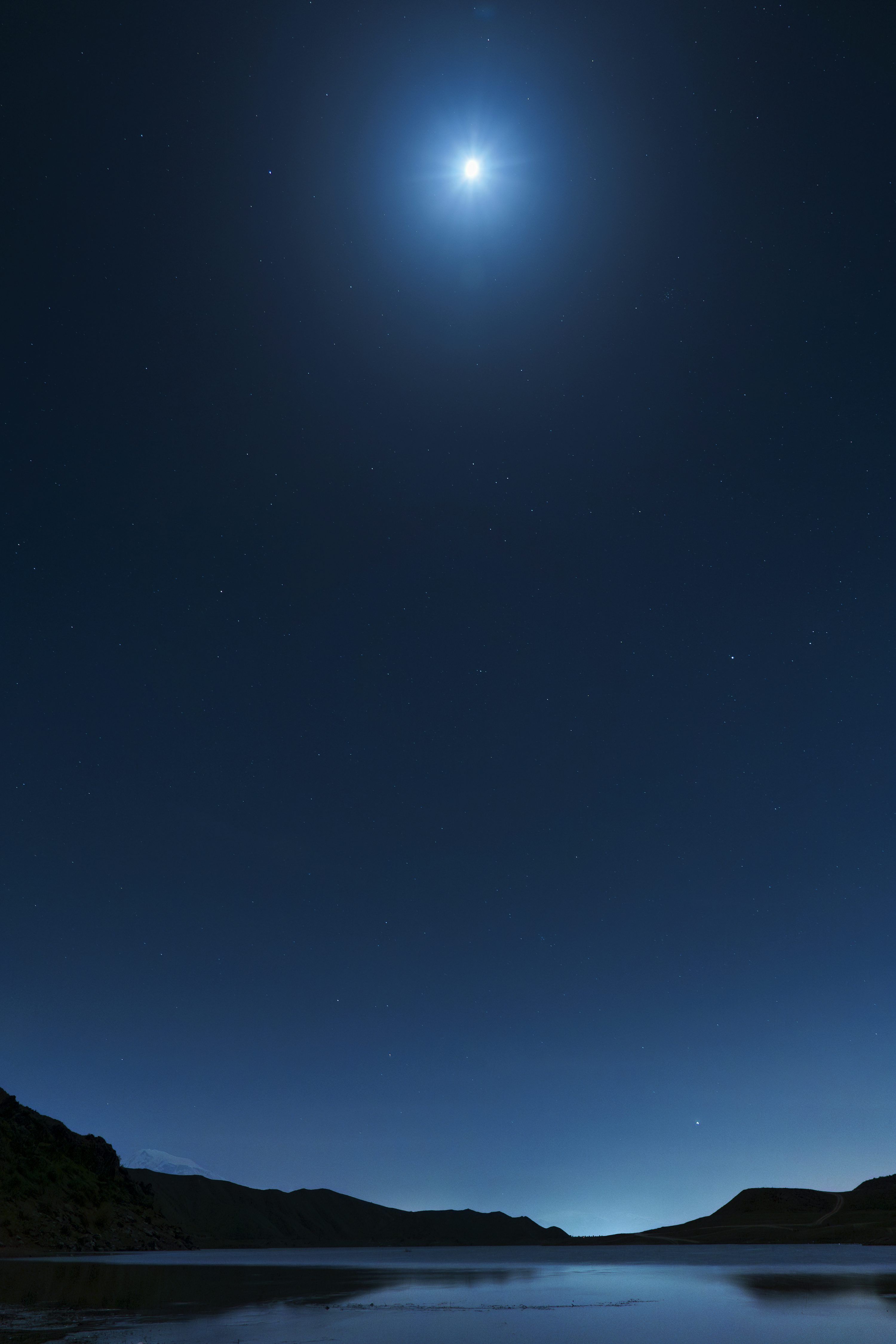 3000x4500 A bright moon shines in the night sky over a lake photo