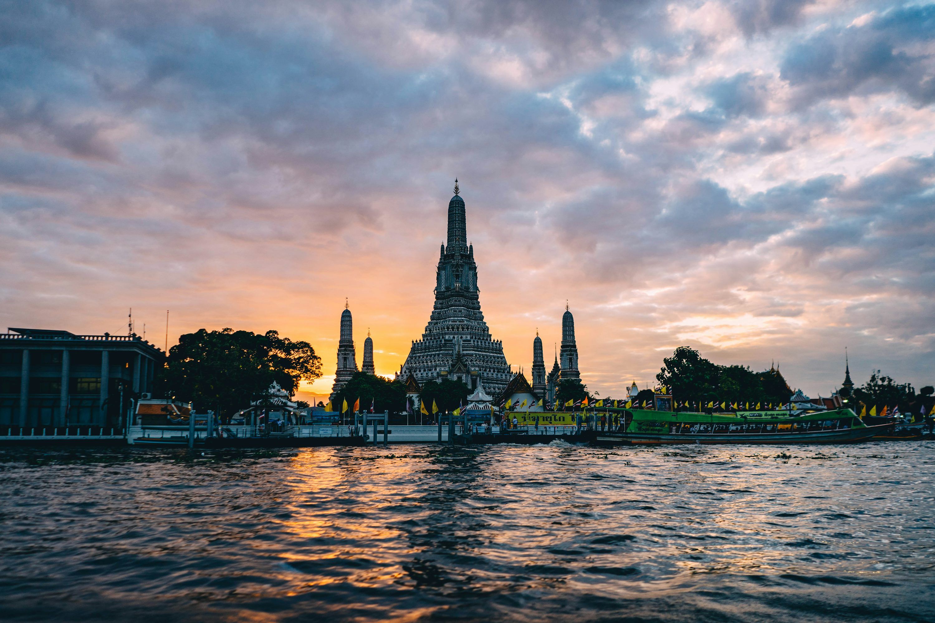 3000x2000 A large building with pointy towers by a body of water with Wat Arun in the background photo