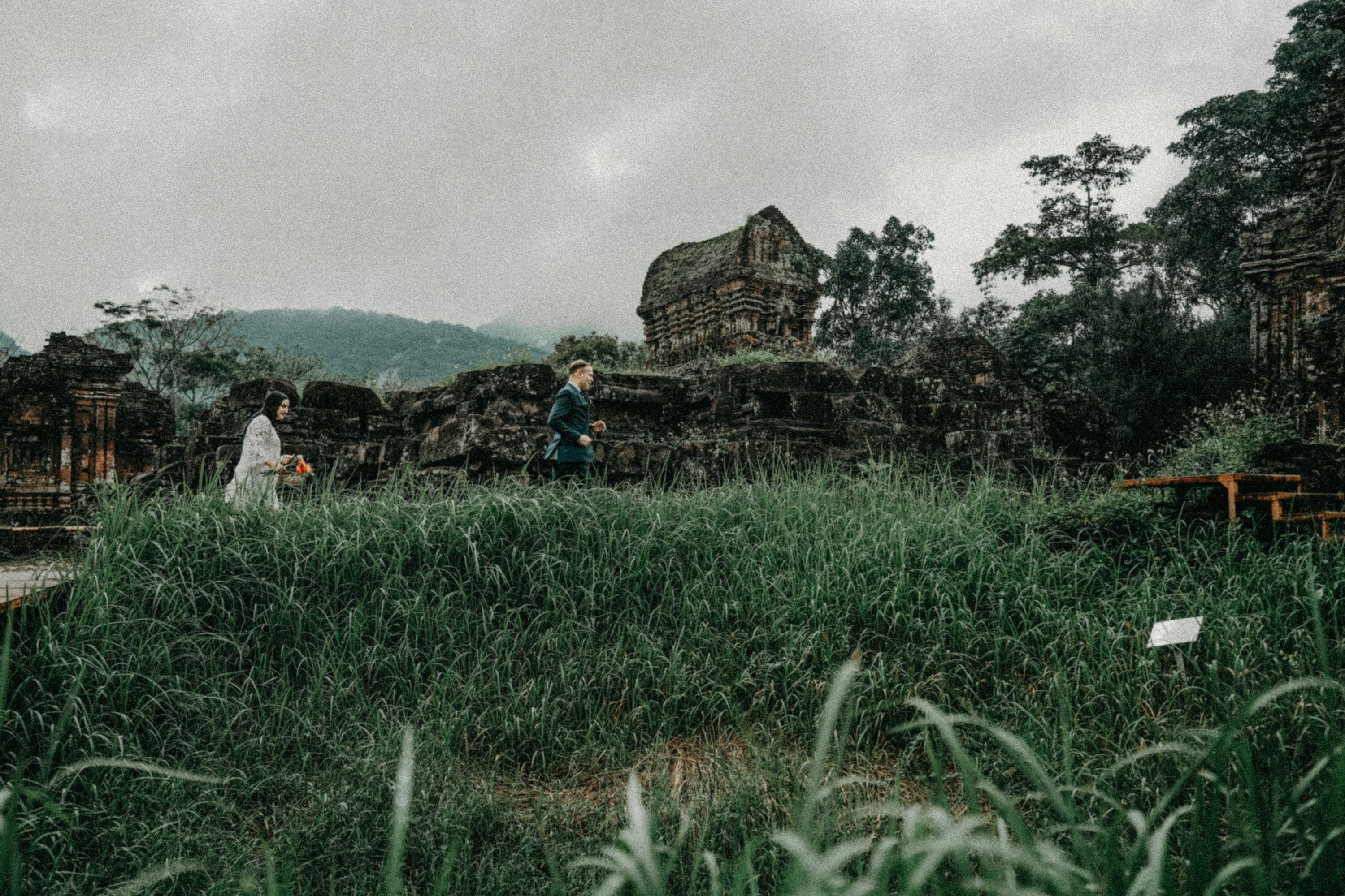 3000x2000 Two people walk past ancient ruins overgrown with grass. photo