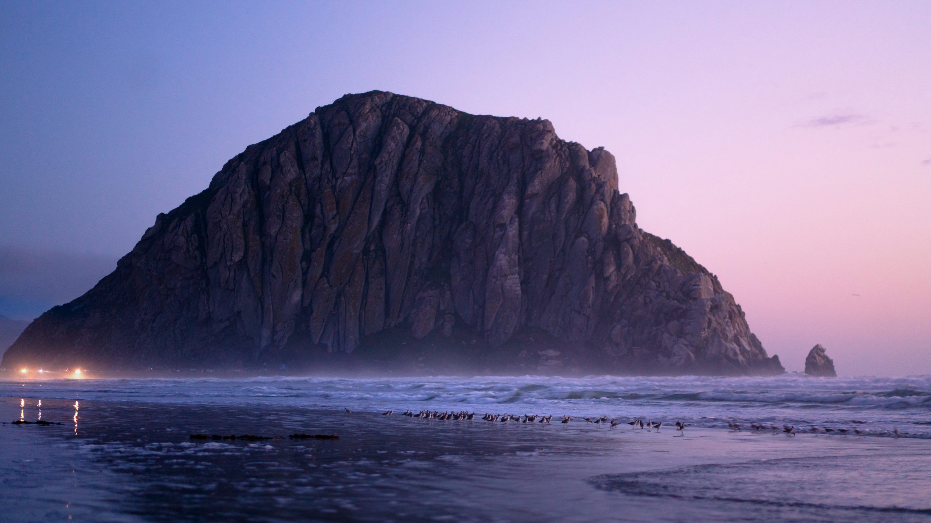 3000x1687 A large rock sticking out of the ocean next to a beach photo