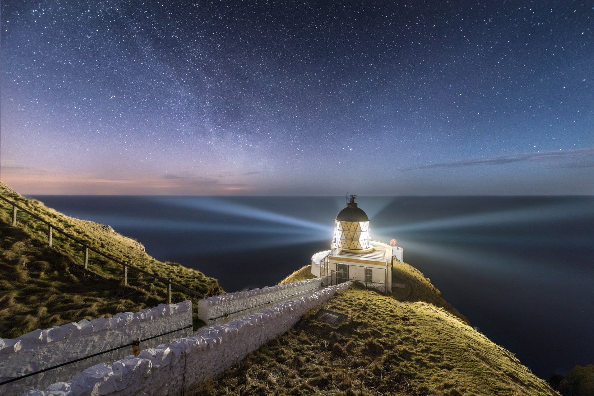 1920x1280 Guiding Light Beneath a Starry Night Sky Over the Ocean