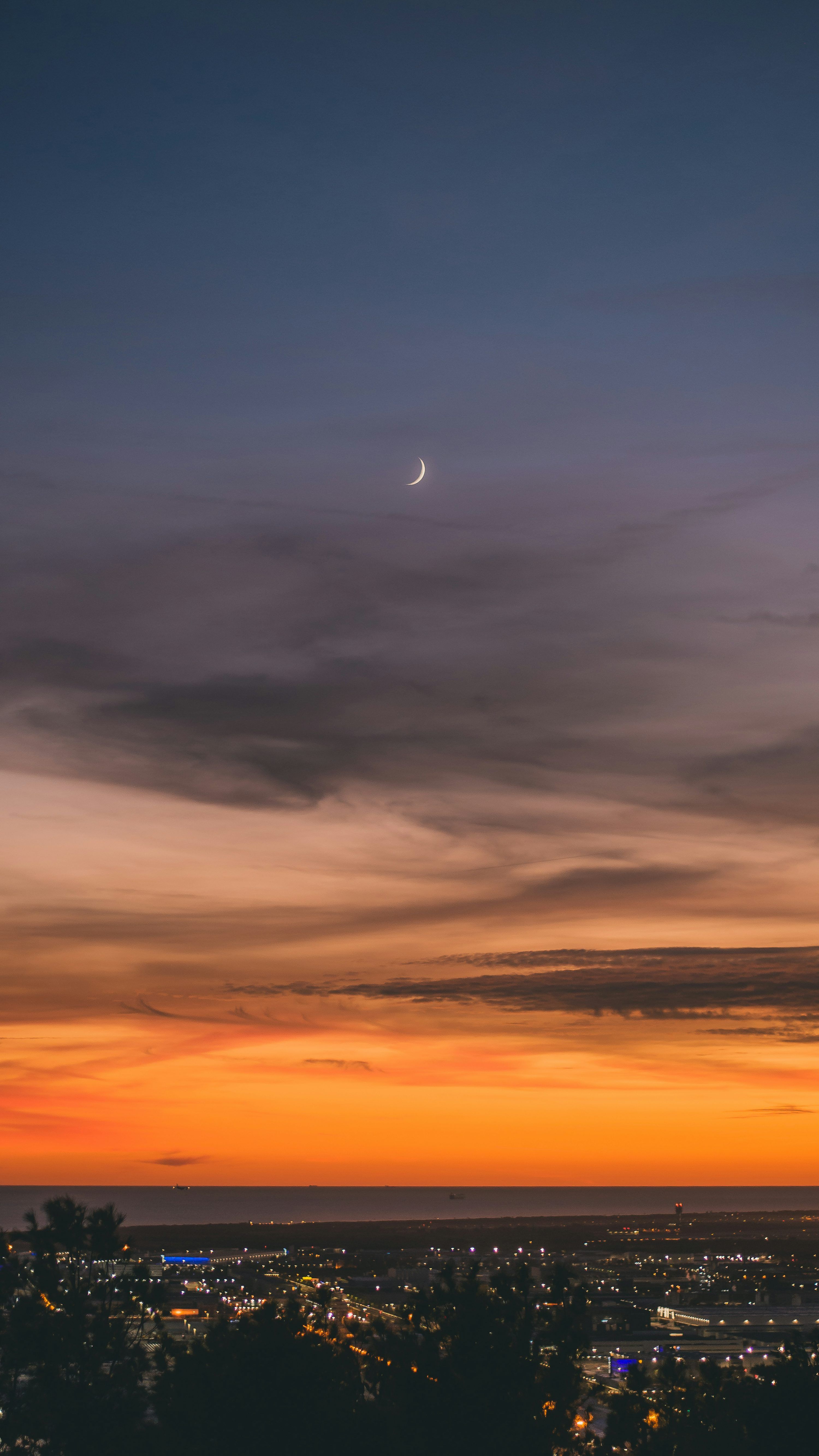 3000x5333 A view of a city at sunset with the moon in the distance photo