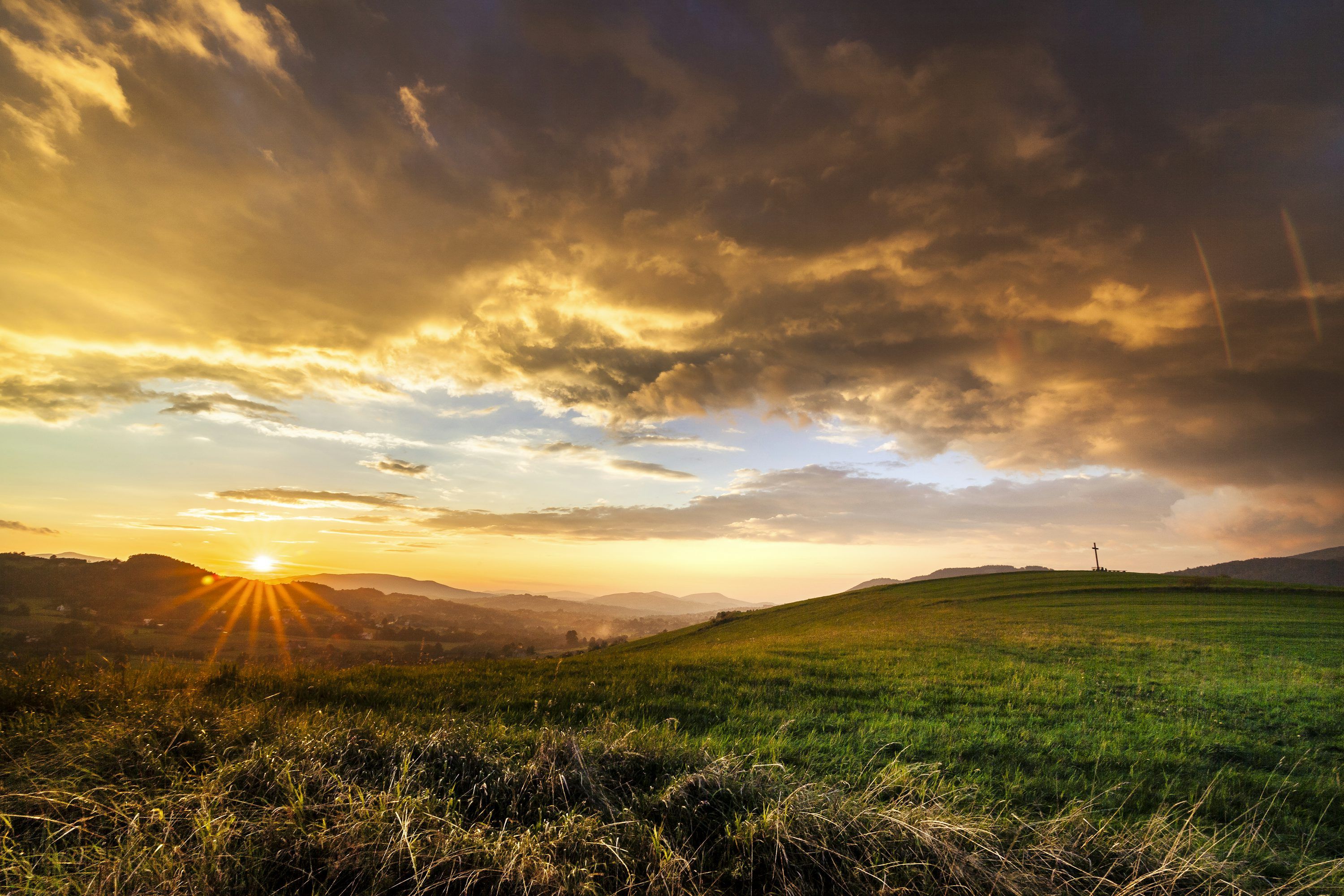 3000x2000 The sun is setting over a grassy hill photo