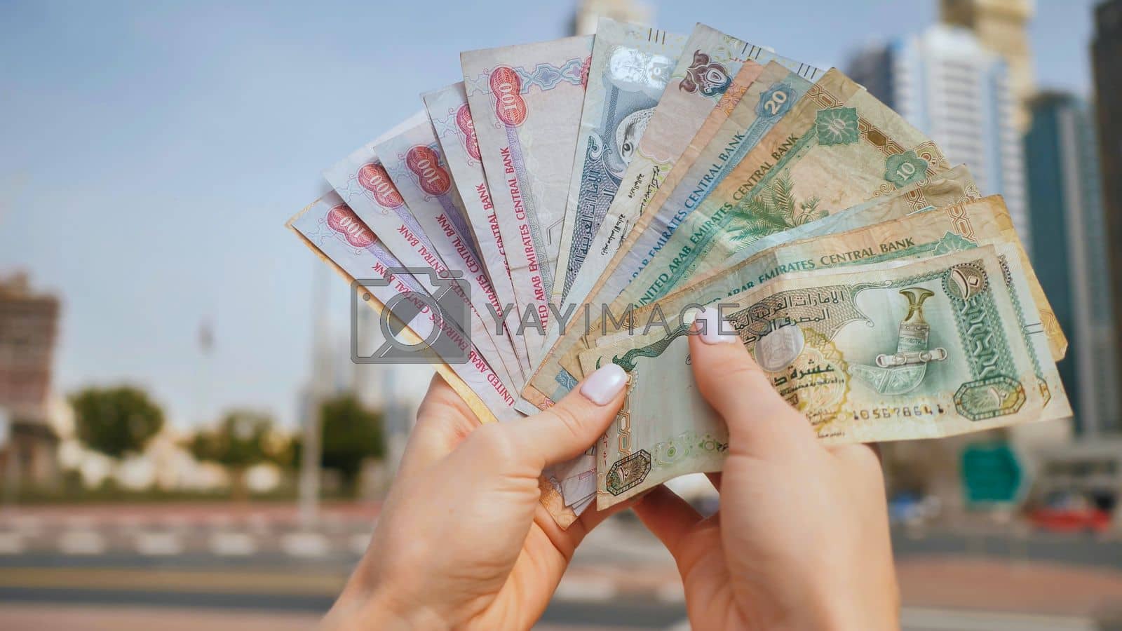 1600x900 Hands of a girl holding money of the United Arab Emirates on the background of Dubai skyscrapers. by DovidPro Vectors & Illustrations with Unlimited Downloads