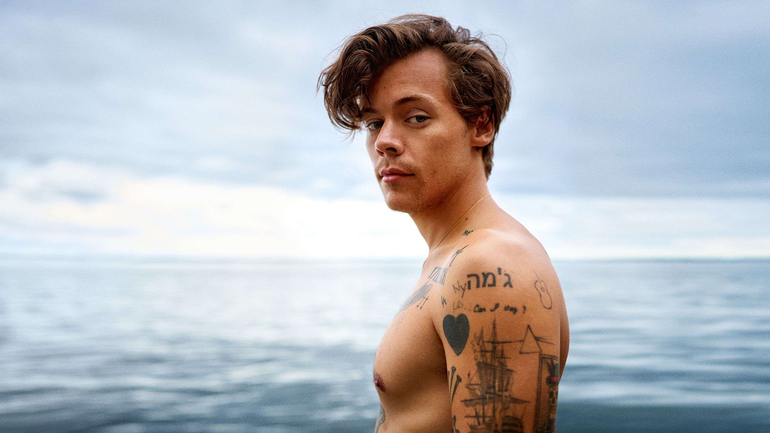 2560x1440 Side View Of Harry Styles With Tattoos Is Standing In Beach Background HD Harry Styles Wallpaper