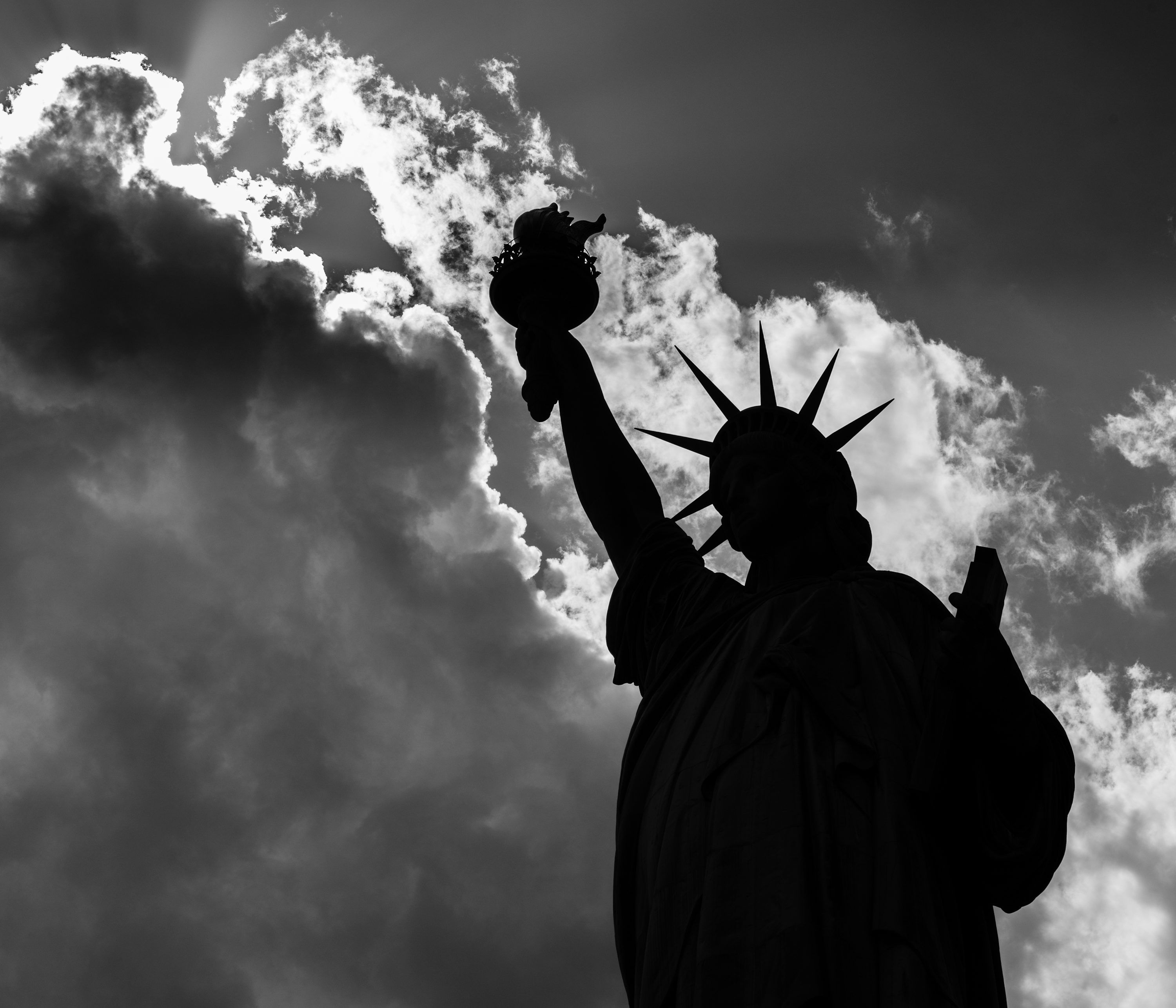 3000x2572 The statue of liberty is silhouetted against a cloudy sky photo