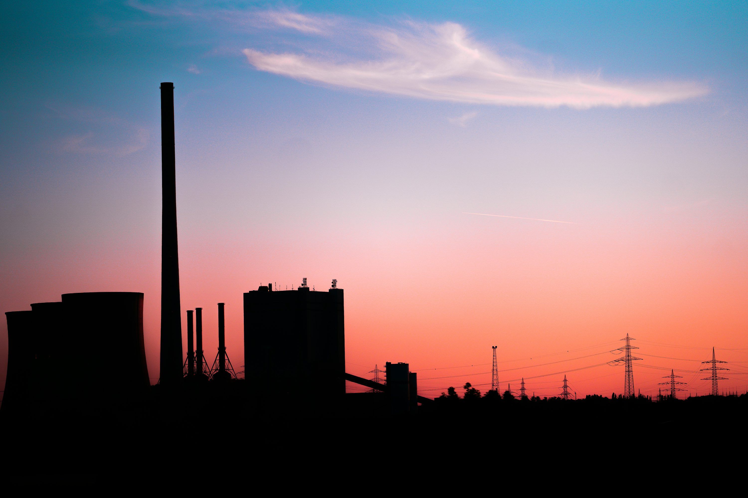 3000x2000 A silhouette of a factory at sunset with power lines in the background photo