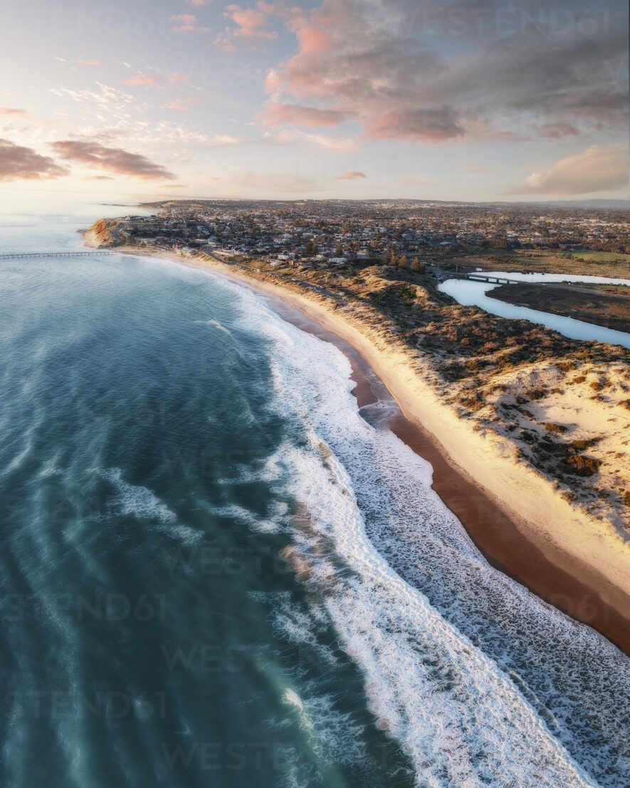 885x1106 Aerial view of long sandy stretch of beach during sunset, with blue water waves rolling onto shore, a river and pink sunset clouds in the background, Port Noarlunga, South Australia, Australia. stock