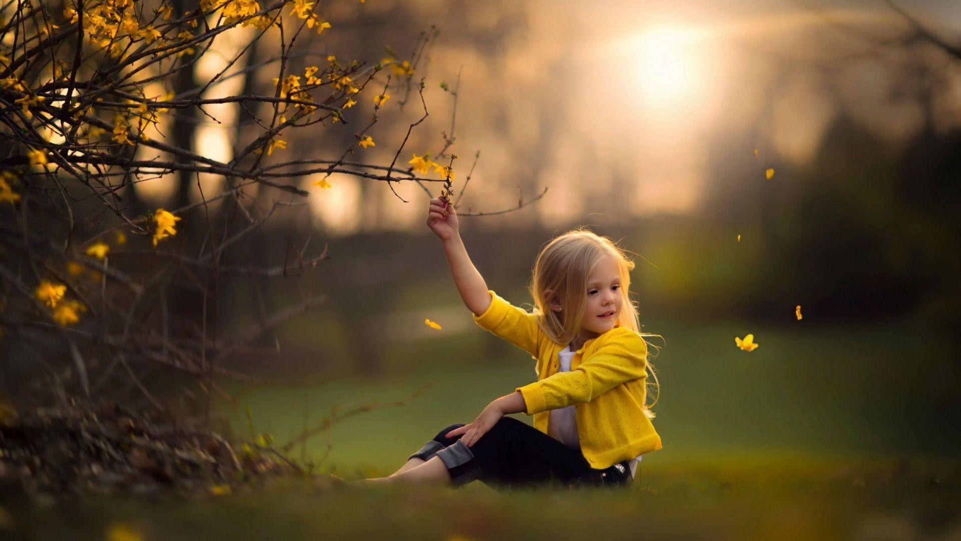 1920x1080 cute baby girl is sitting on green grass touching flower wearing yellow dress with sunlight background HD cute Wallpaper