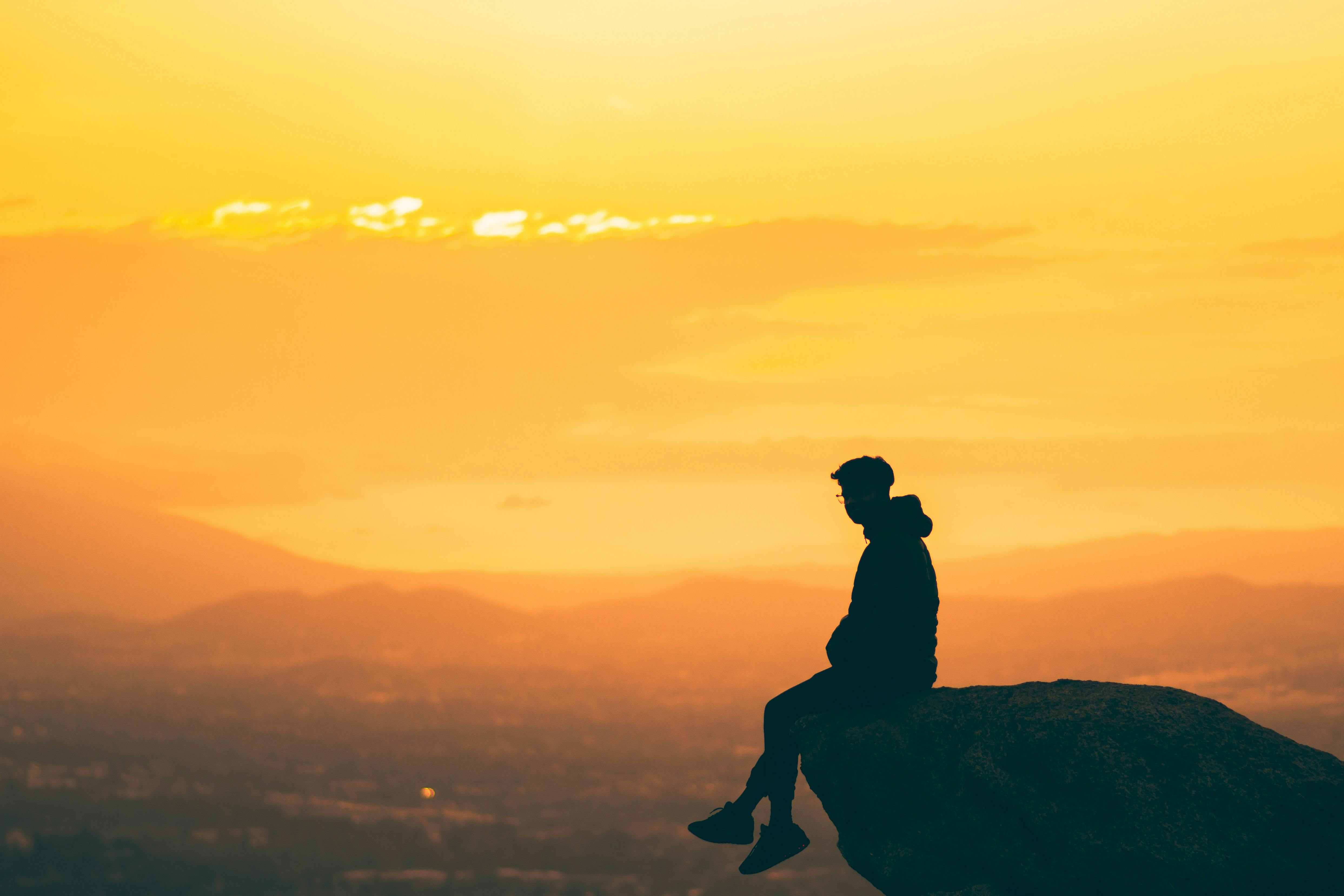 4971x3314 Silhouette of a Person Sitting at the Edge of a Rock at Sunset · Free