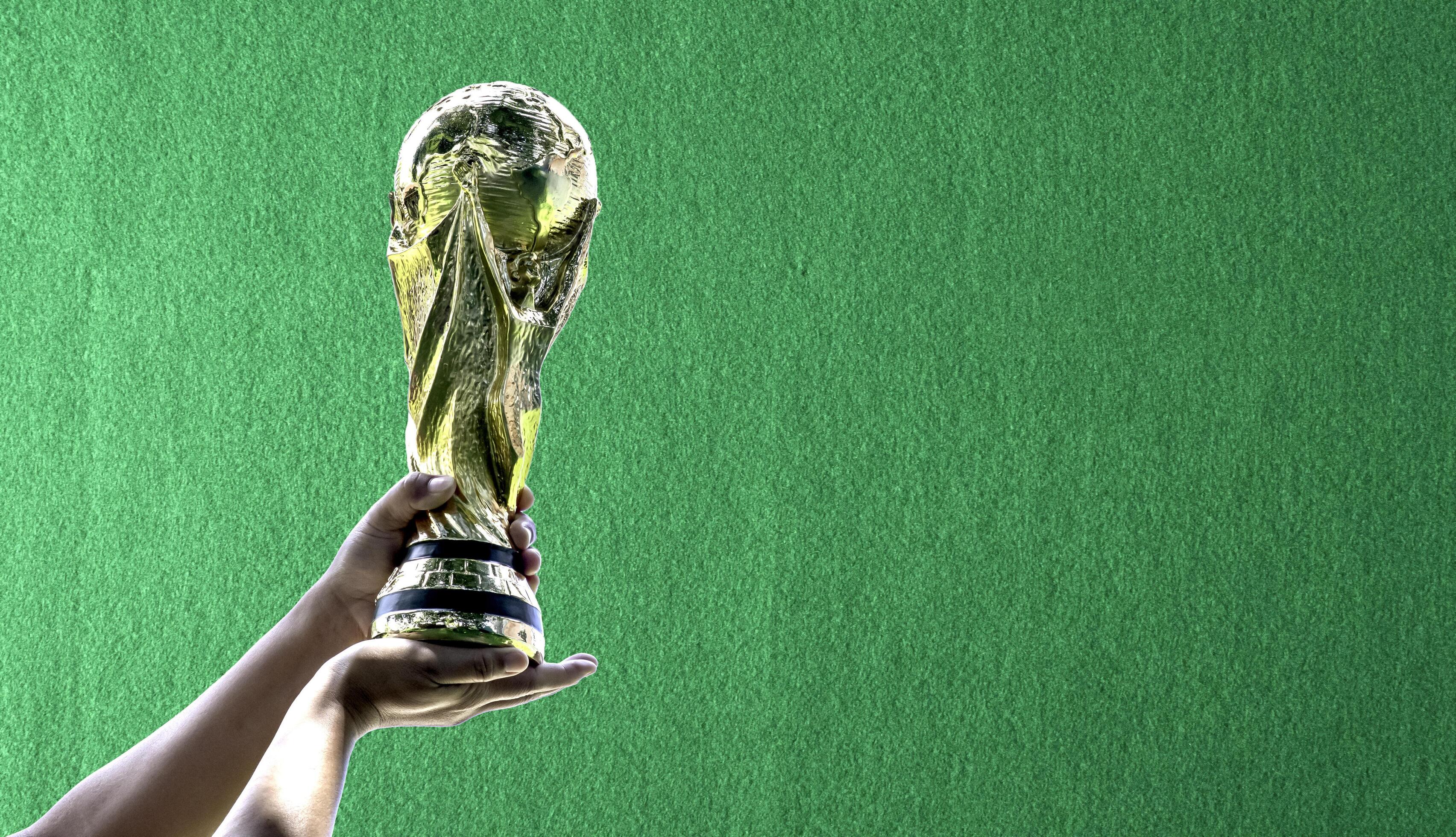 3409x1960 World Cup with green frieze background. hand holding a World Cup winner trophy. The concept for World Cup in Qatar. Copy space on left for design