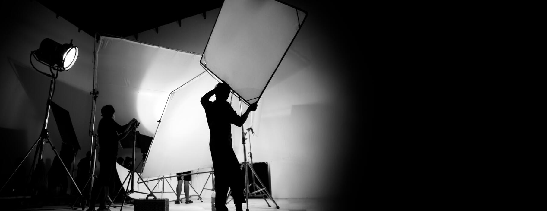 1814x700 Silhouette of video production behind the scenes or B roll or making of TV commercial movie that film crew team lightman and cameraman working together with director in big studio with pro
