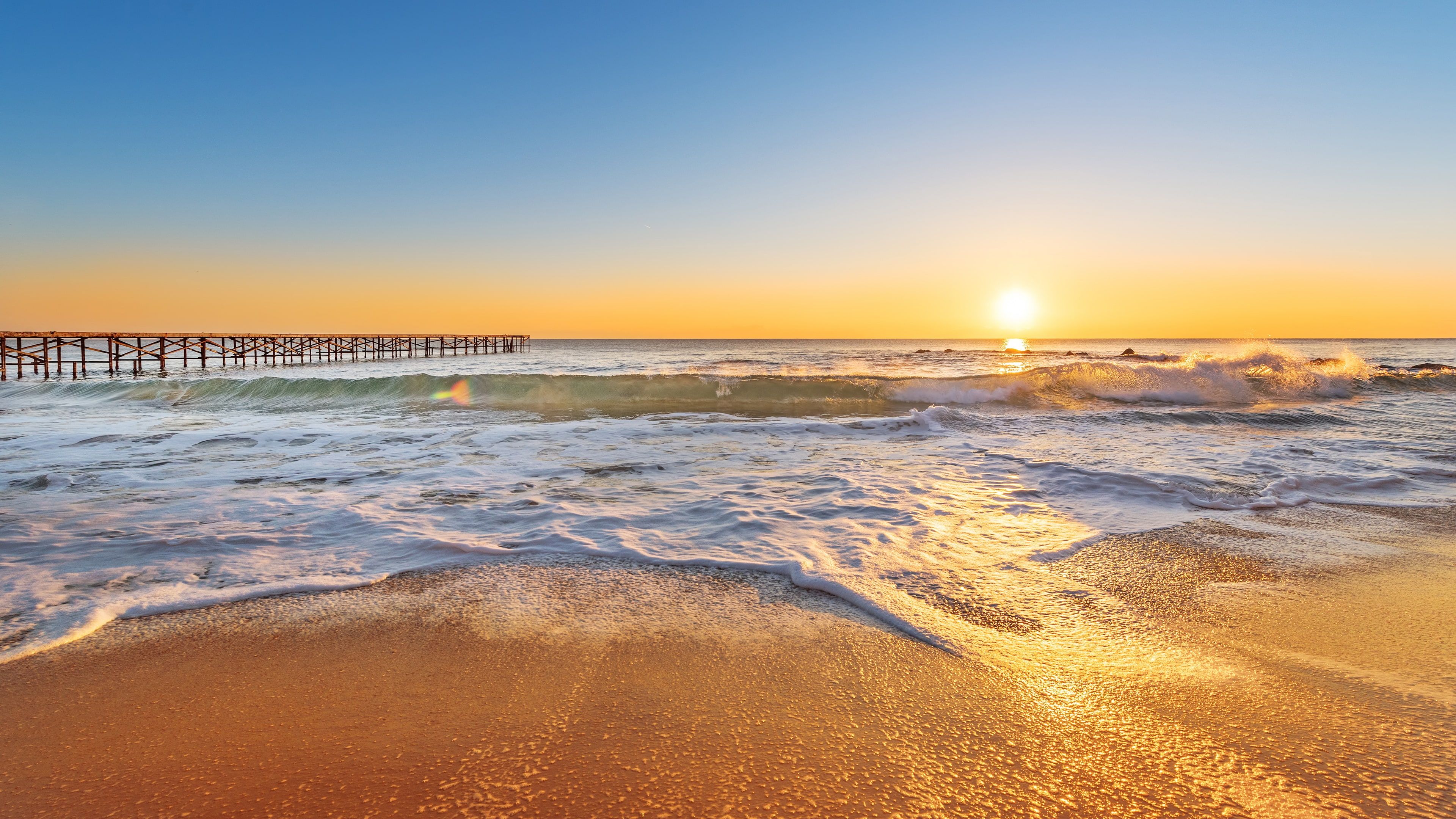 3840x2160 Ocean Waves Pier Beach Sand In Blue Yellow Sky Background During Sunrise 4K HD Ocean Wallpaper