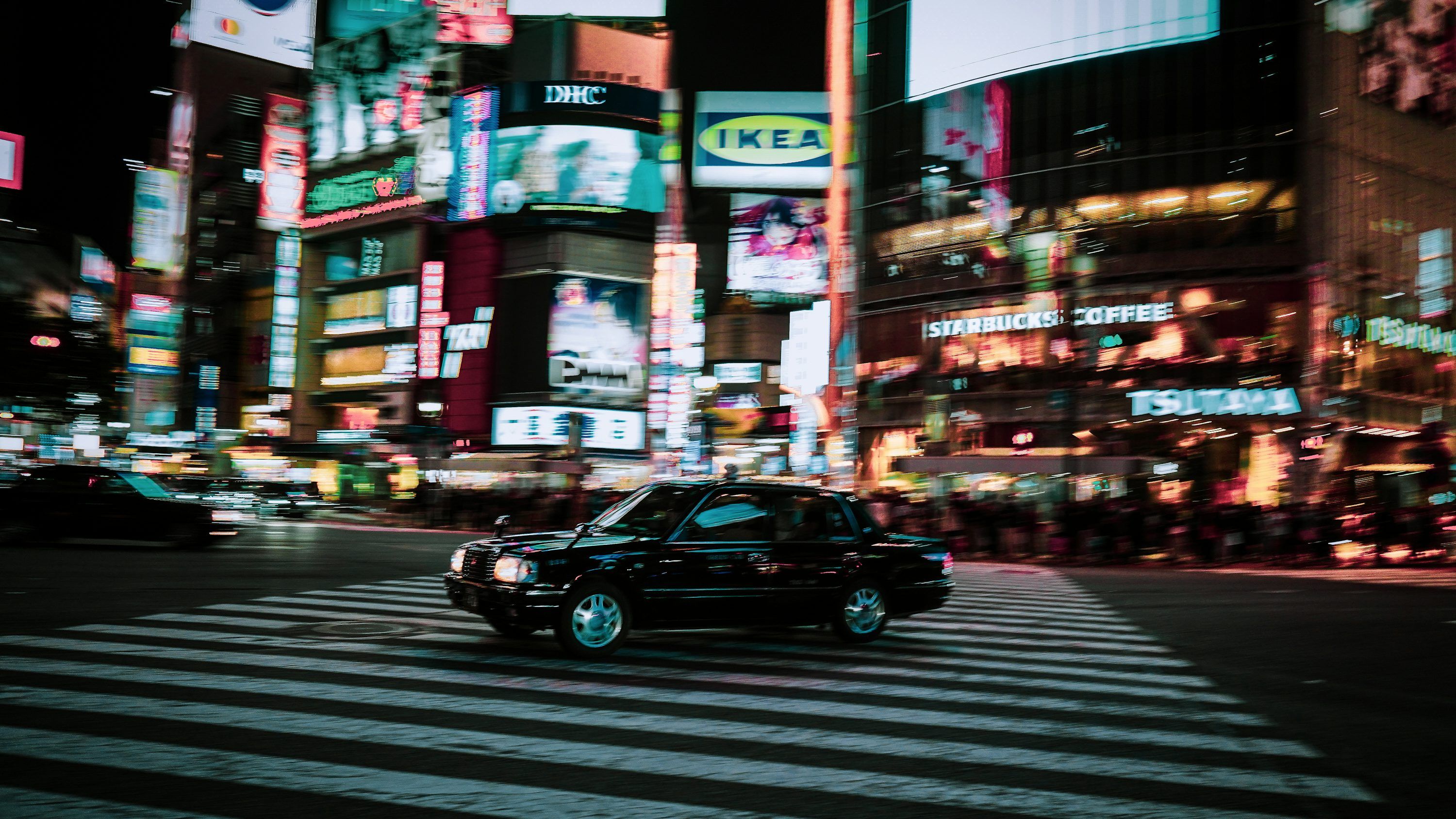 3000x1688 A black car driving down a street next to tall buildings photo
