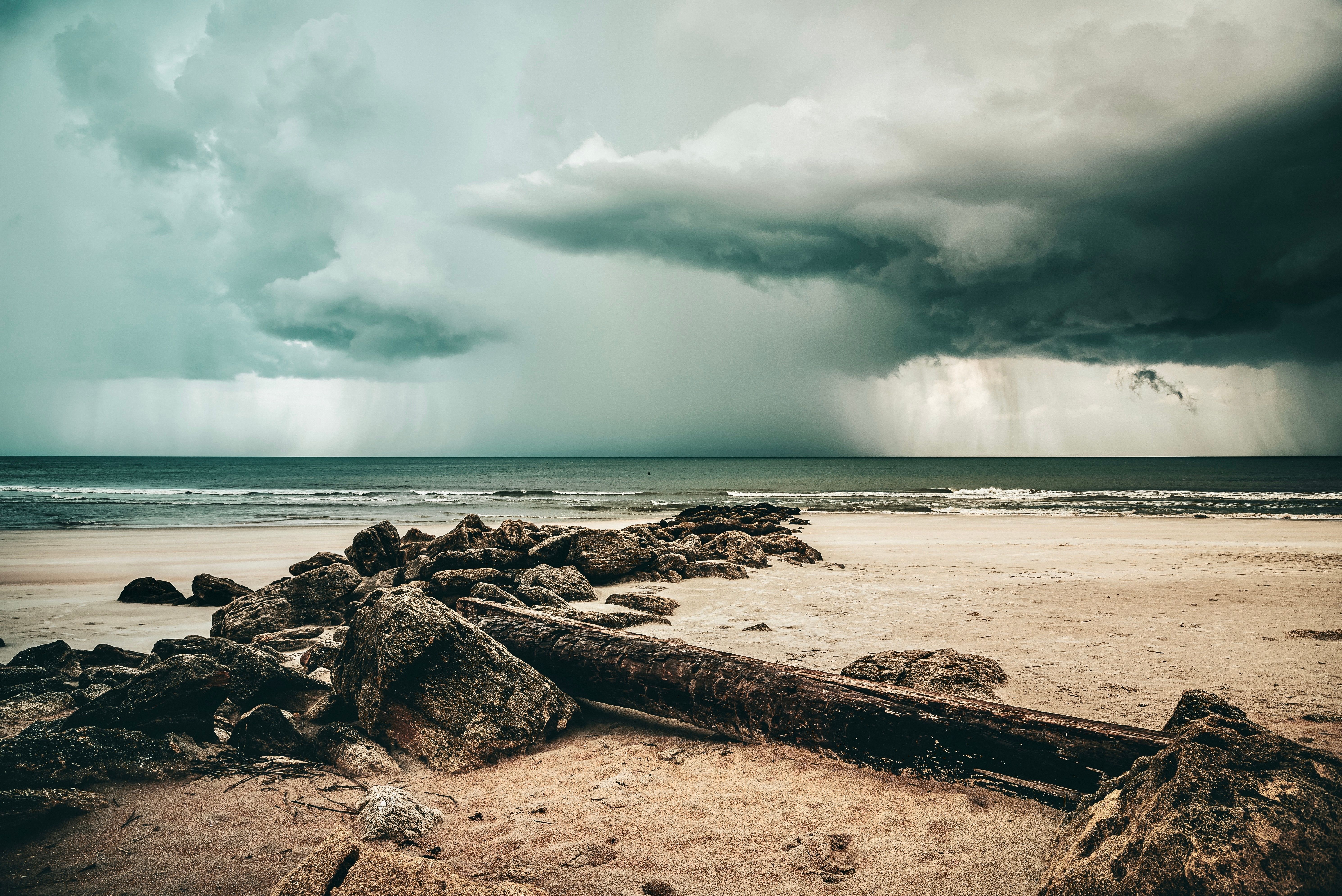 5960x3979 Rocks and a Tree Log on the Beach under a Stormy Sky · Free
