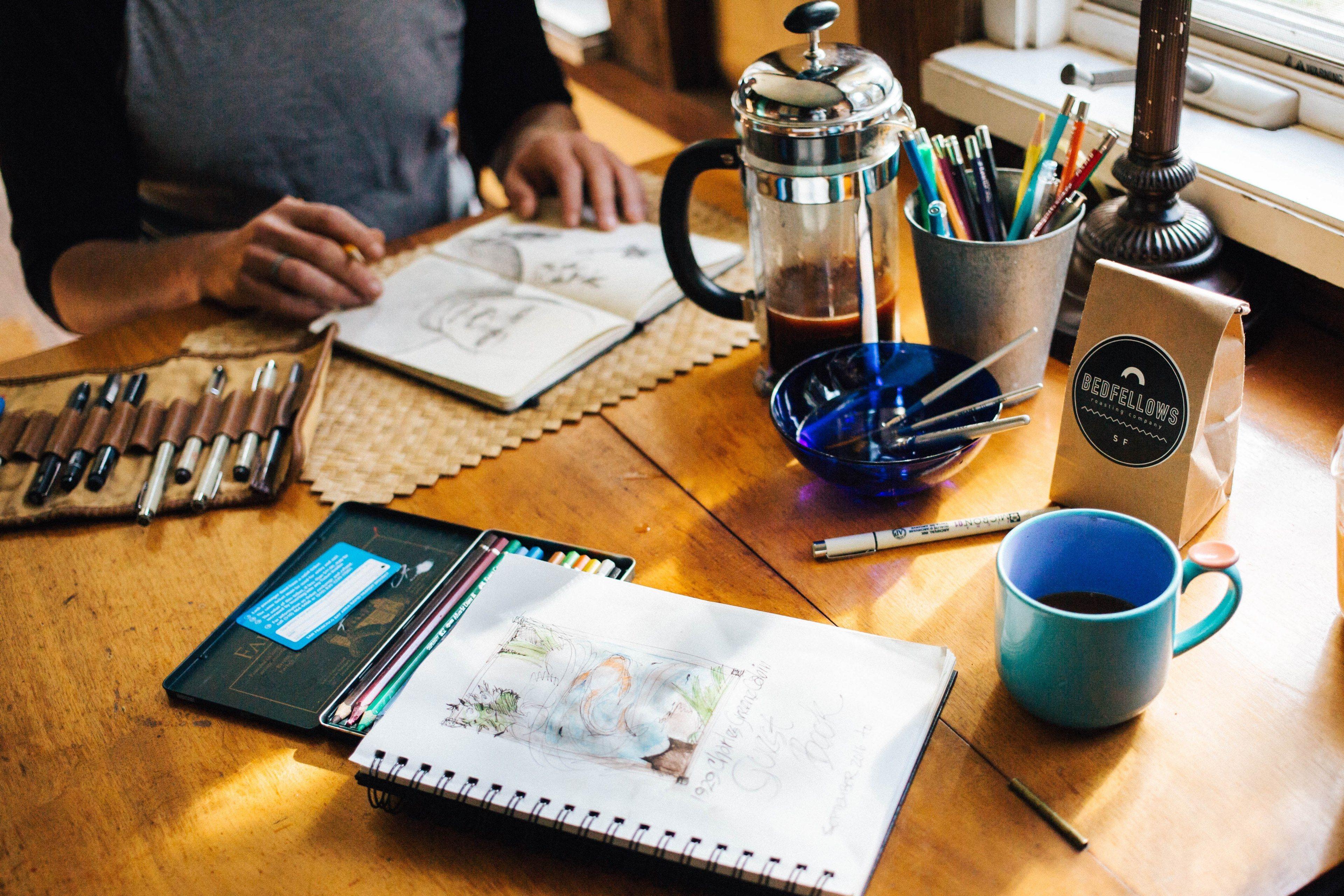 3840x2560 a man looking at sketches in a notebook at a table with a cup