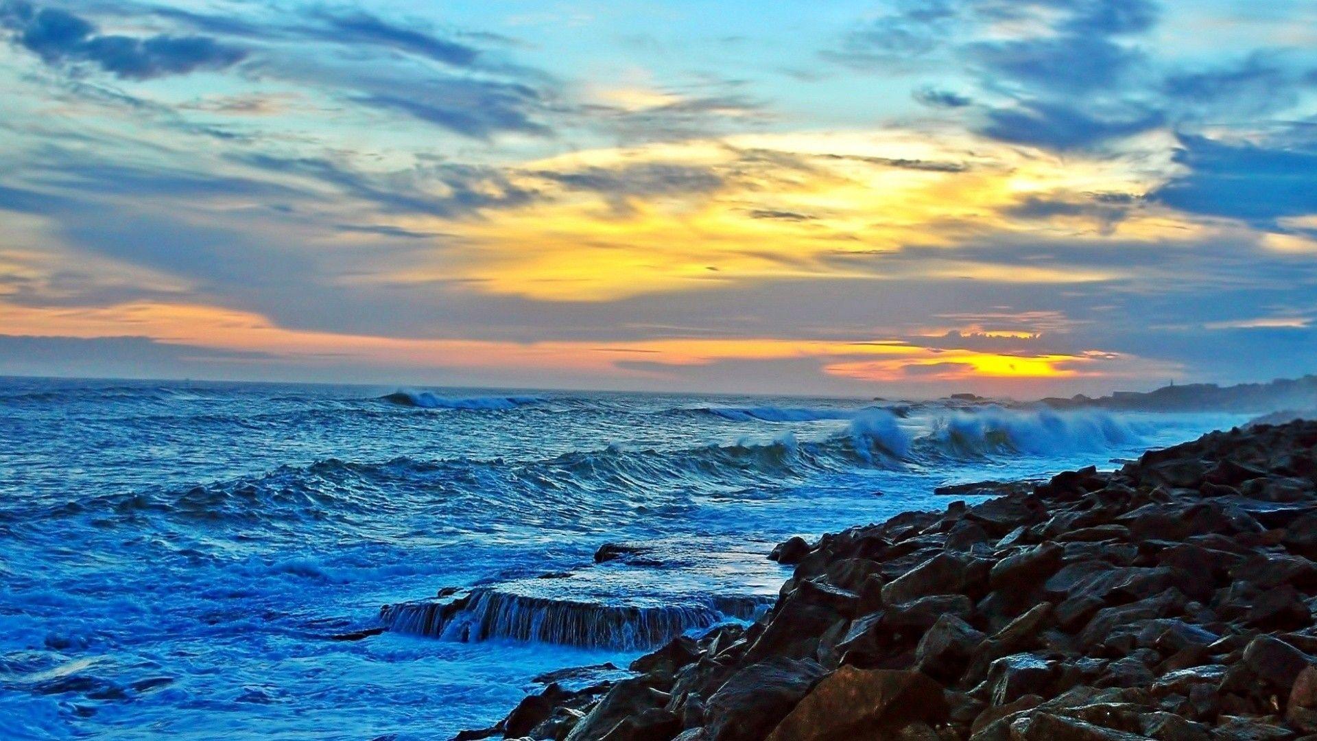 1920x1080 Beach Angry Sea Rocky Coast Sunset Clouds Waves Surf Rocks Nature