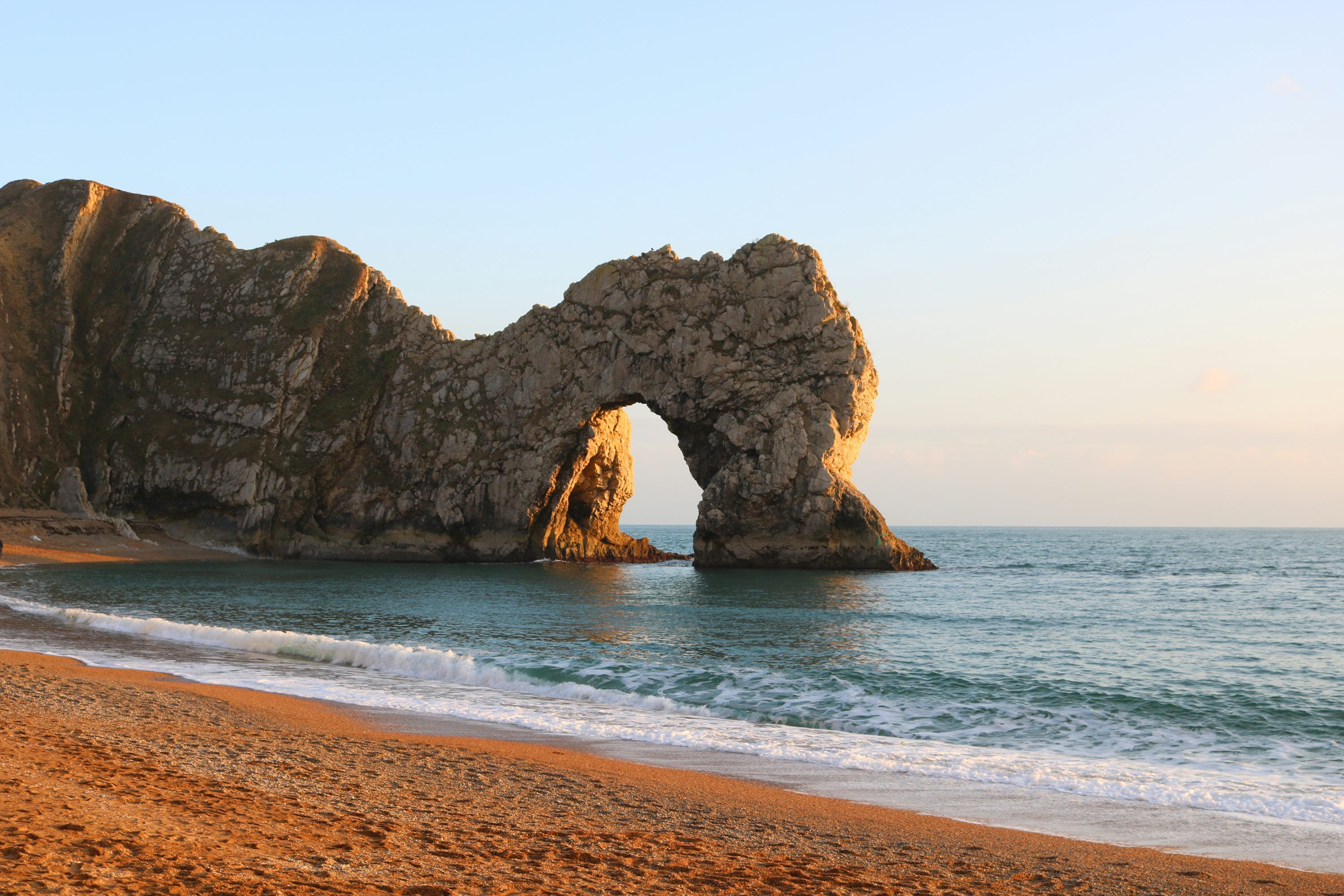 3000x2000 A view of a beach with a rock arch in the water photo