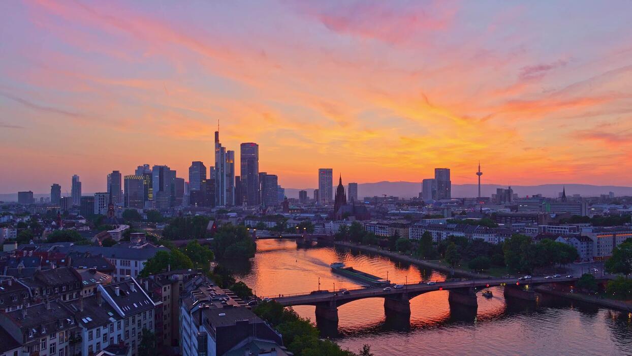 1244x700 Frankfurt Downtown Skyline, Residential Buildings, Bridges and Barge on Main River at Fiery Sunset Evening Twilight. Aerial View. Hesse, Germany