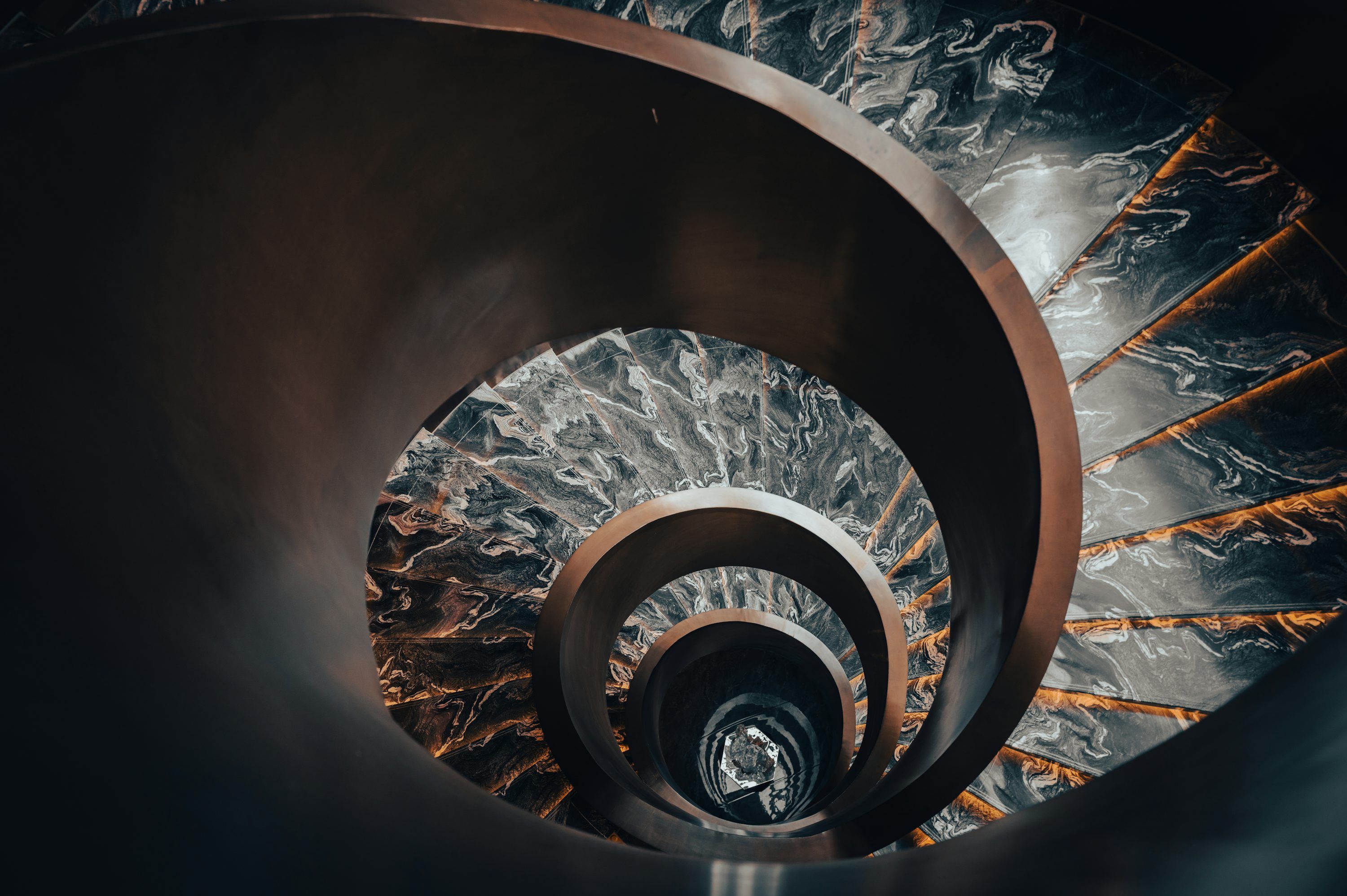 3000x1997 Dark spiral staircase with marble accents descends into darkness photo