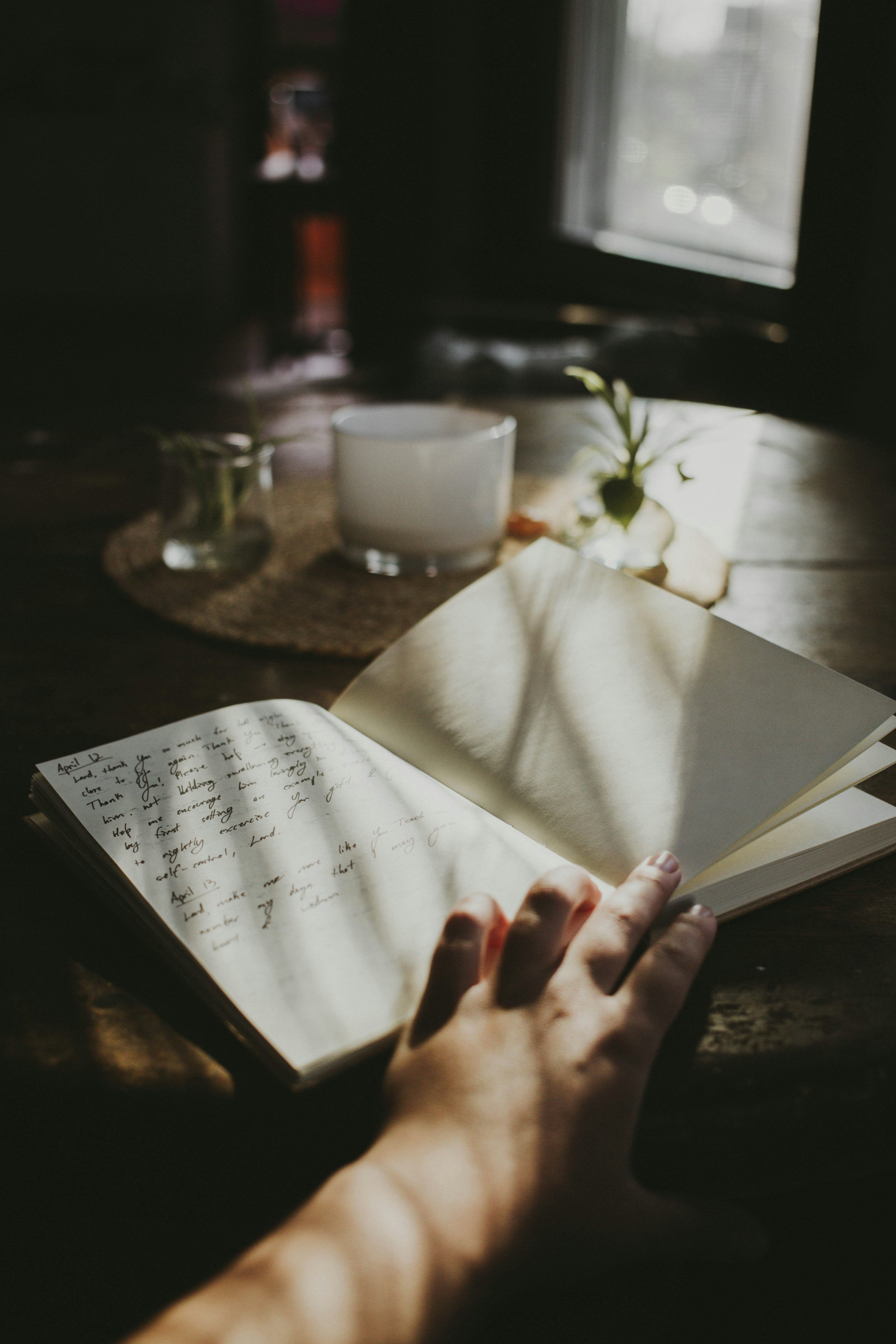 3000x4500 A person's hand holding an open book on a table photo