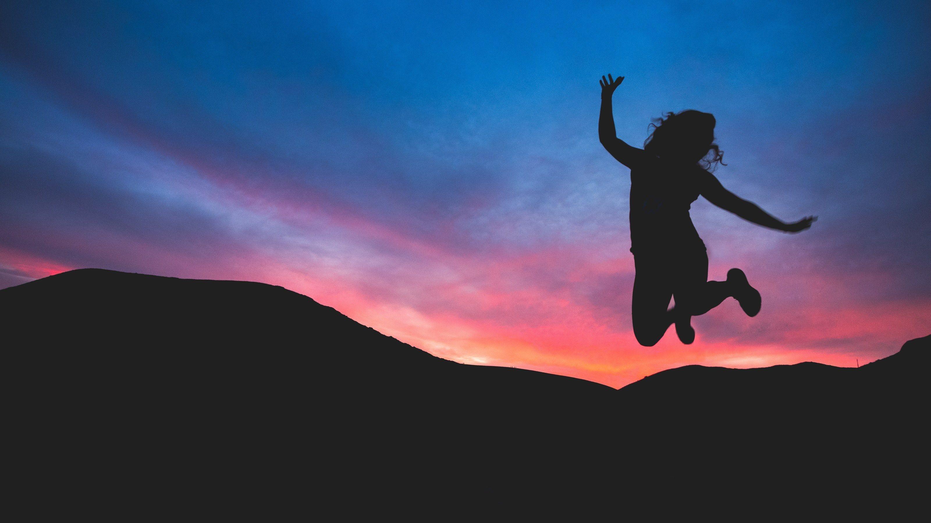 3200x1800 a woman in silhouette jumps for joy against dark mountains and a