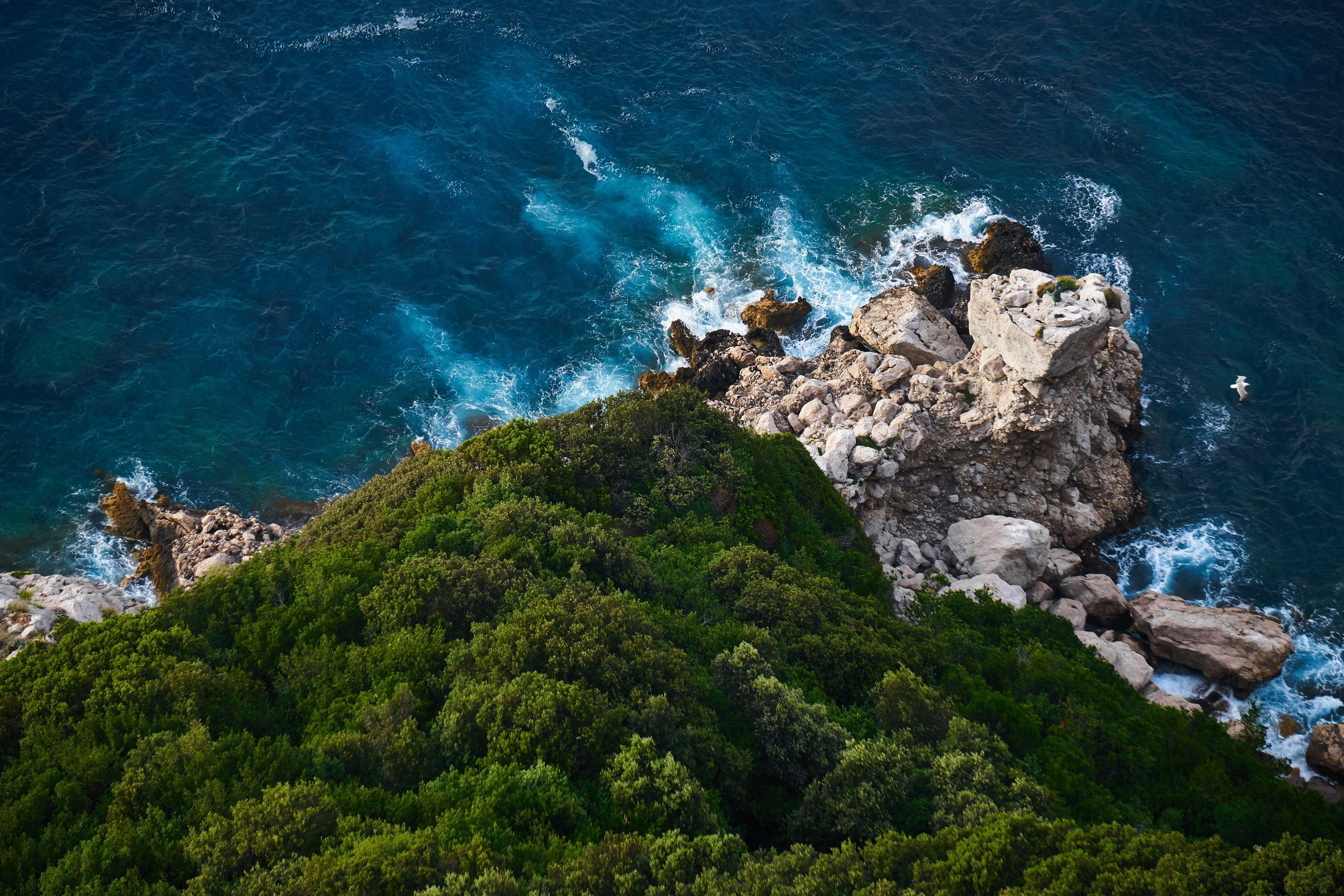 3840x2560 a drone shot of a wooded cliff over a rough searocky cliff