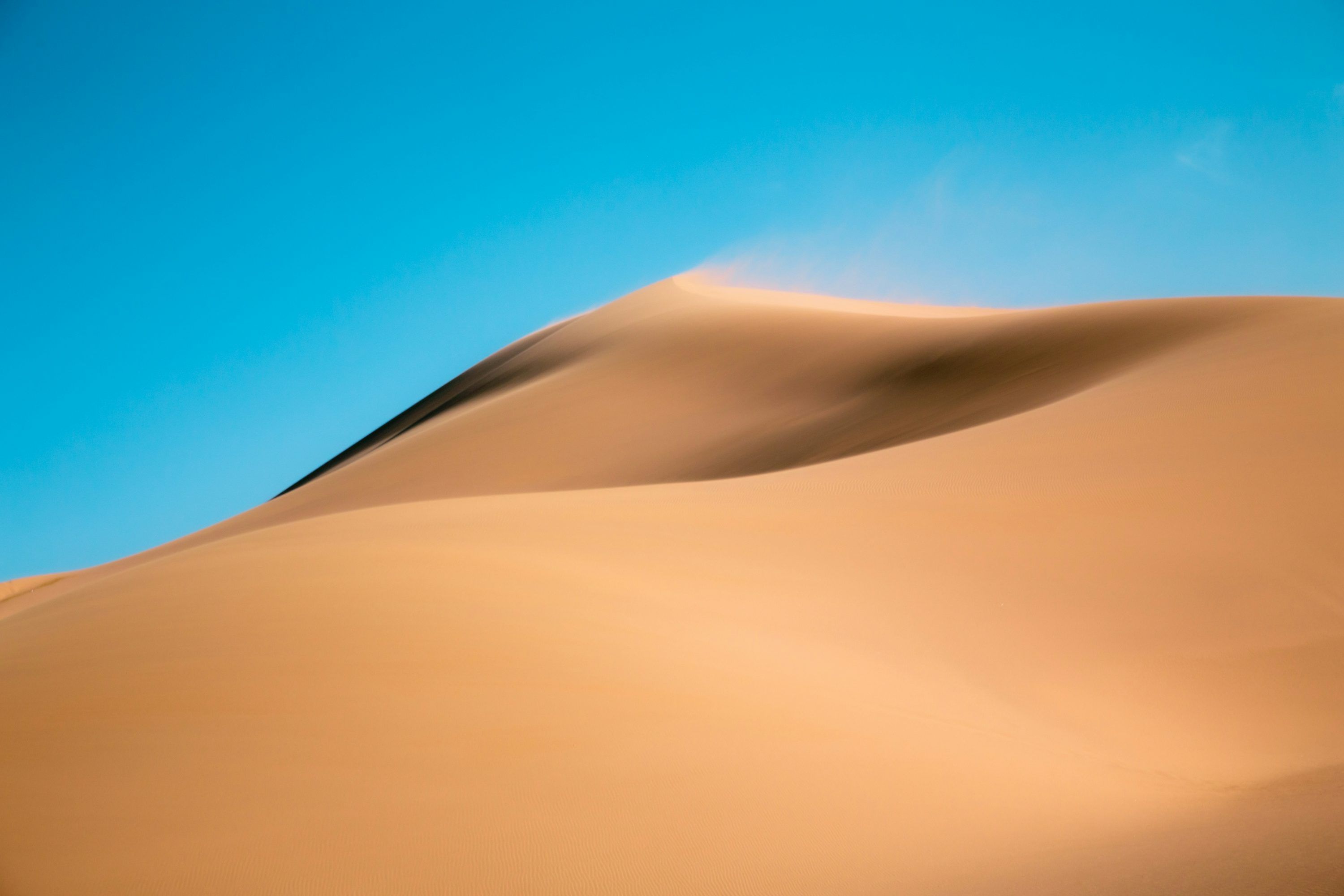 3000x2000 A large sand dune with a blue sky in the background photo