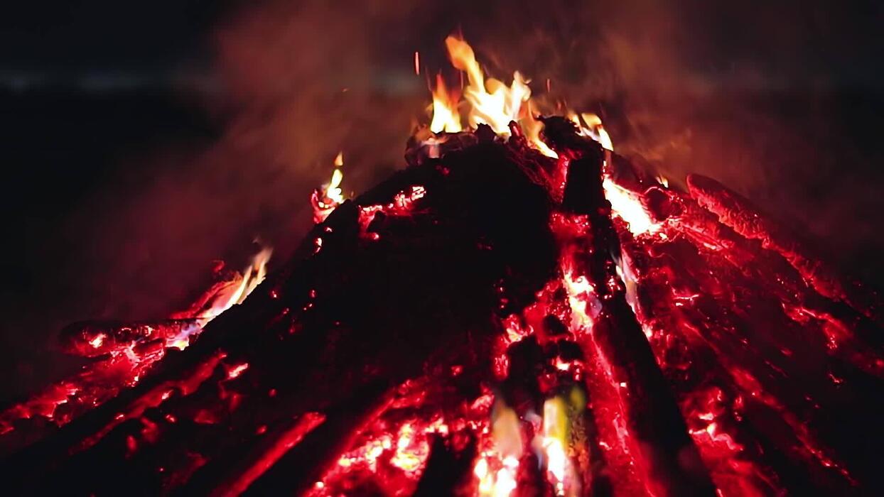 1244x700 Big Campfire is Burning Down in Early Morning or Evening against the Blue Sky. Wood on Fire. Flying Sparks. Travel and Tourism Concept. Remains of a Giant Bonfire at Summer Shot, Timelapse