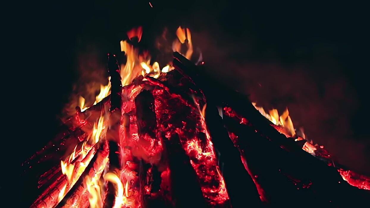 1244x700 Big Campfire is Burning Down in Early Morning or Evening against the Blue Sky. Wood on Fire. Flying Sparks. Travel and Tourism Concept. Remains of a Giant Bonfire at Summer Static Shot, Timelapse